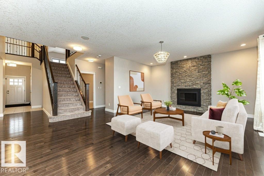 Living area with stairs, a fireplace, a textured ceiling, dark wood-type flooring, and a chandelier - 3198 Winspear Crescent Sw, Edmonton, AB - Indoor Photo Showing Living Room With Fireplace