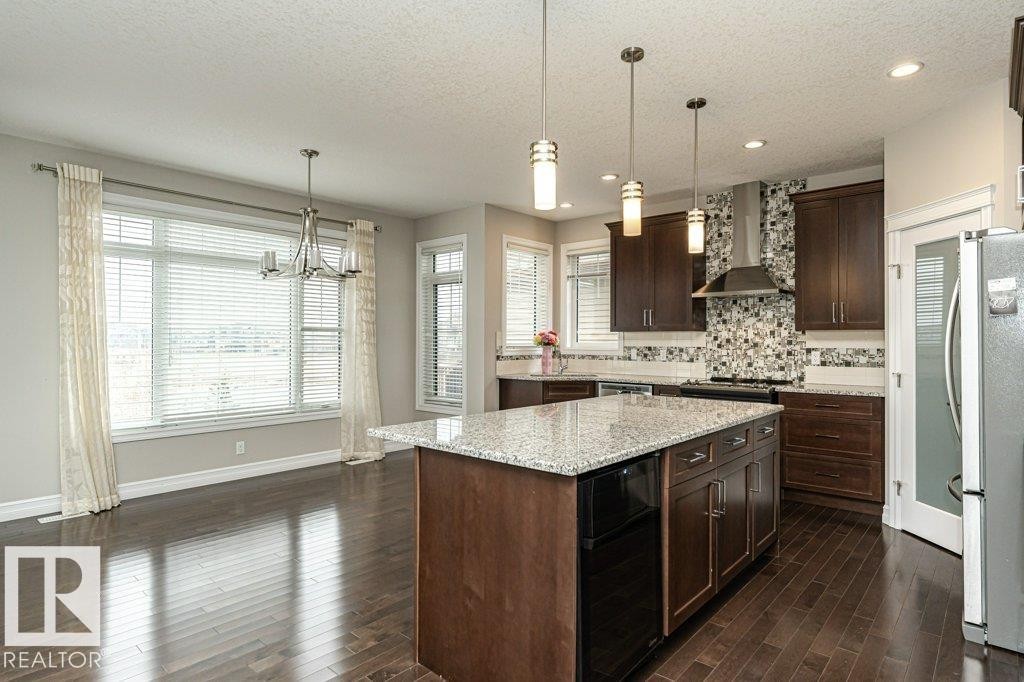 Kitchen with tasteful backsplash, pendant lighting, freestanding refrigerator, wall chimney exhaust hood, and a textured ceiling - 3198 Winspear Crescent Sw, Edmonton, AB - Indoor Photo Showing Kitchen With Upgraded Kitchen
