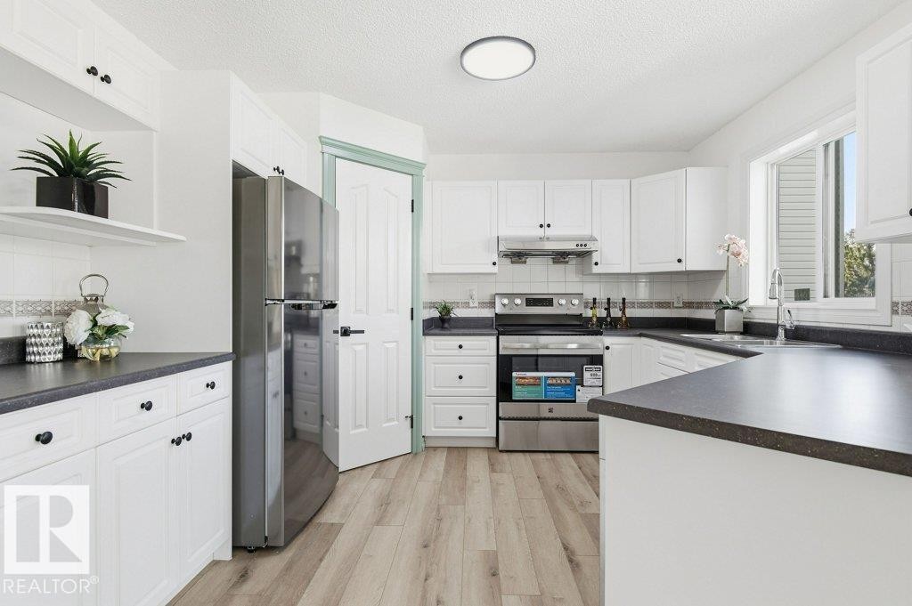 Kitchen with stainless steel appliances, dark countertops, white cabinets, light wood finished floors, and a textured ceiling - 1112 118A Street Nw, Edmonton, AB - Indoor Photo Showing Kitchen
