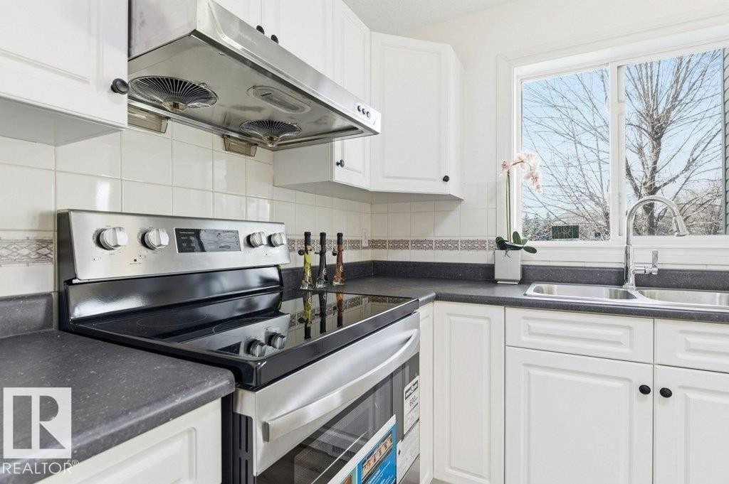 Kitchen featuring electric stove, under cabinet range hood, white cabinetry, and tasteful backsplash - 1112 118A Street Nw, Edmonton, AB - Indoor Photo Showing Kitchen With Double Sink