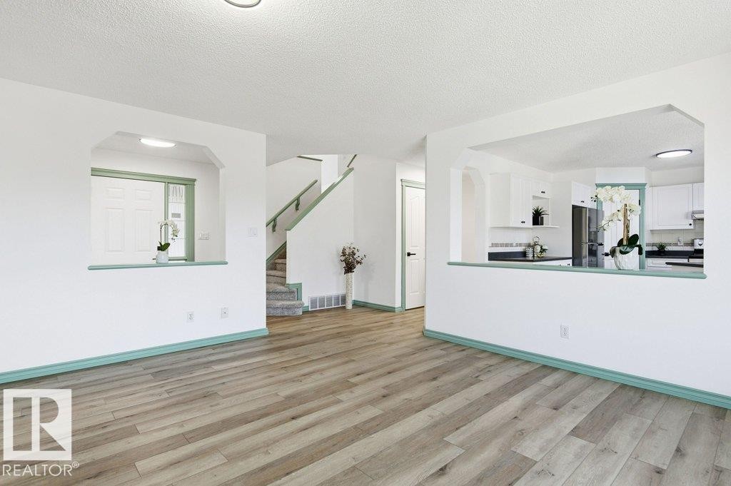 Unfurnished living room with a textured ceiling, light wood finished floors, stairs, and arched walkways - 1112 118A Street Nw, Edmonton, AB - Indoor