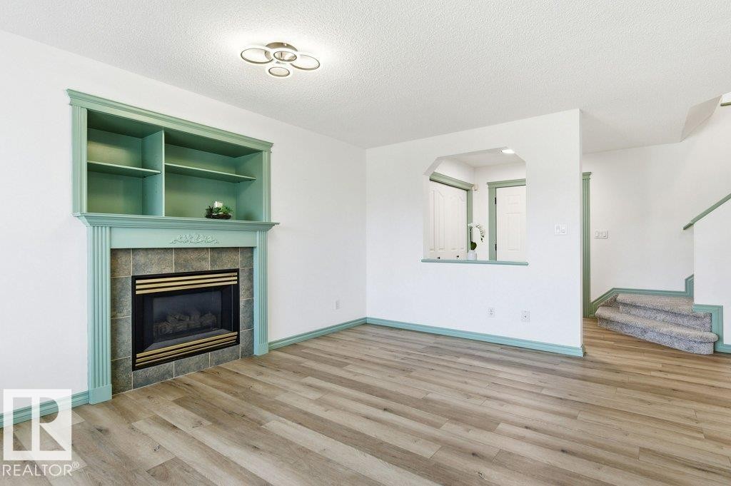 Unfurnished living room featuring a textured ceiling, light wood-style floors, a tiled fireplace, arched walkways, and stairway - 1112 118A Street Nw, Edmonton, AB - Indoor Photo Showing Living Room With Fireplace