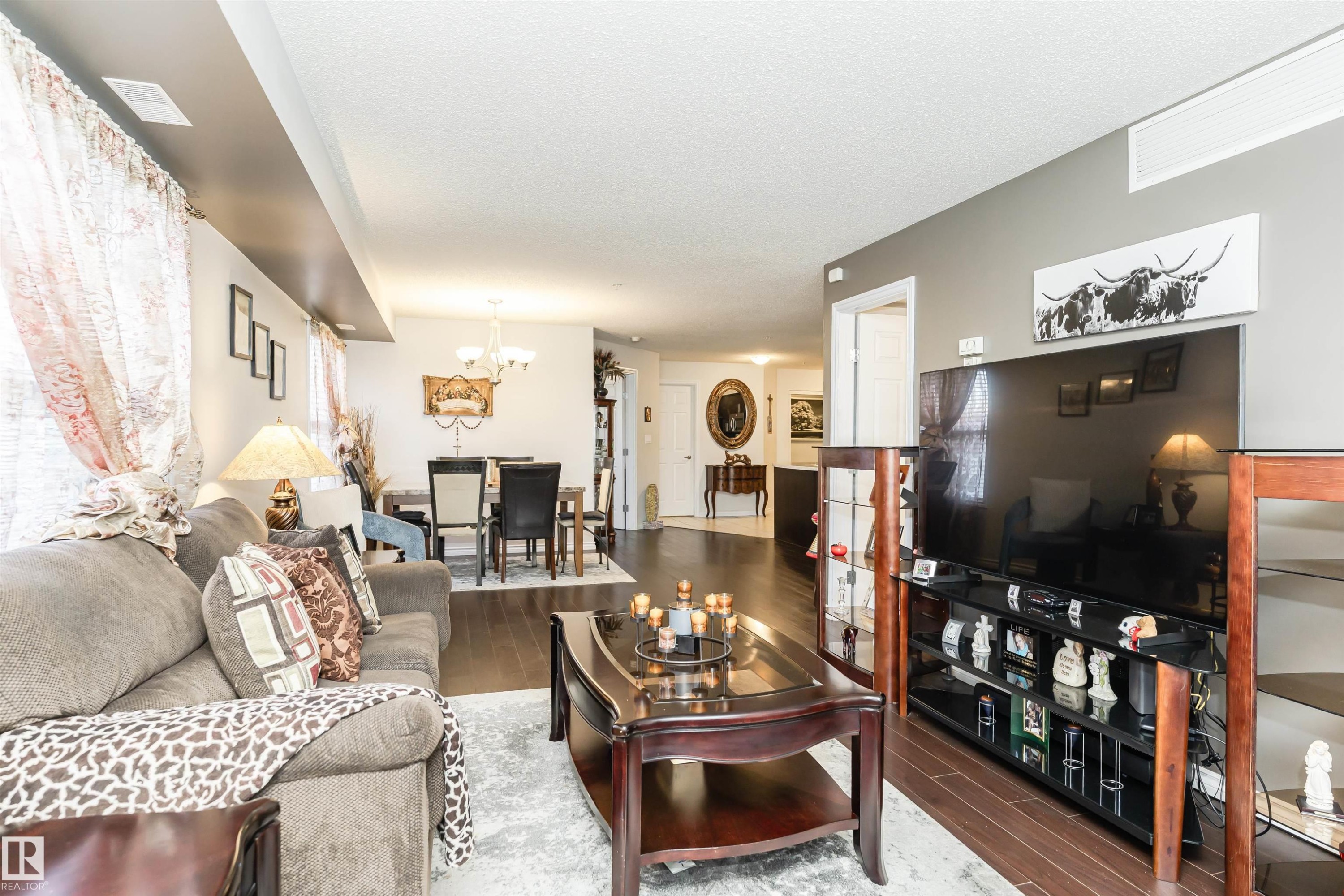 Living room with dark wood finished floors, a chandelier, and a textured ceiling - 107 10118 106 Avenue, Edmonton, AB - Indoor Photo Showing Living Room
