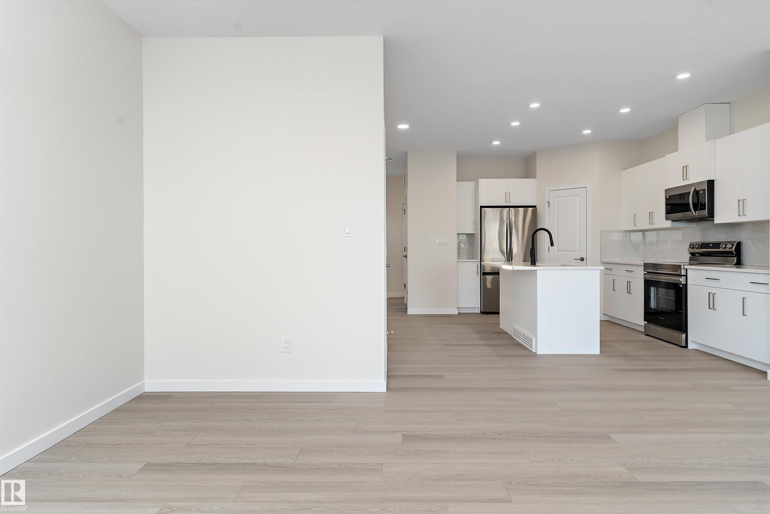 Kitchen featuring a kitchen island with sink, appliances with stainless steel finishes, white cabinetry, light wood-style flooring, and backsplash - 823 Rowan Close, Edmonton, AB - Indoor Photo Showing Kitchen With Upgraded Kitchen