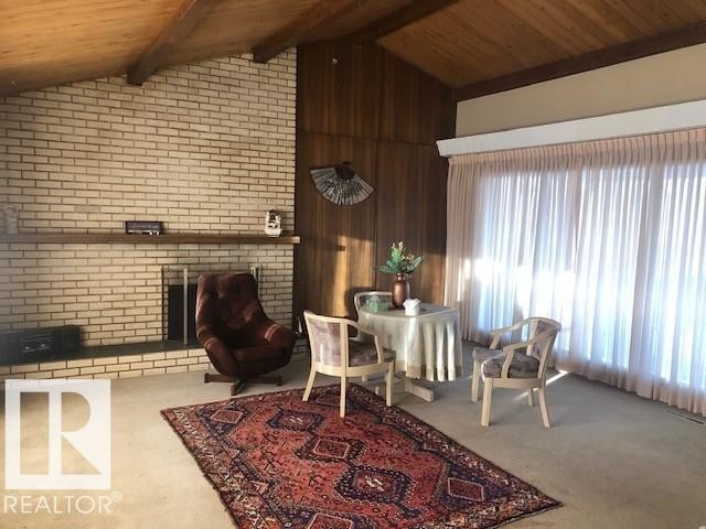 Living area with a fireplace, wood ceiling, carpet flooring, and wooden walls - 4213 42 Avenue, Innisfail, AB - Indoor