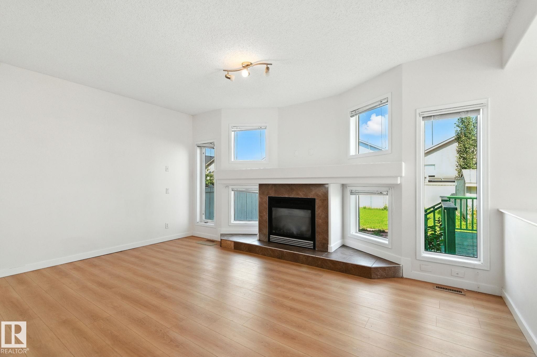 Unfurnished living room with a tiled fireplace, light wood-type flooring, and a textured ceiling - 7836 7 Avenue, Edmonton, AB - Indoor Photo Showing Living Room With Fireplace