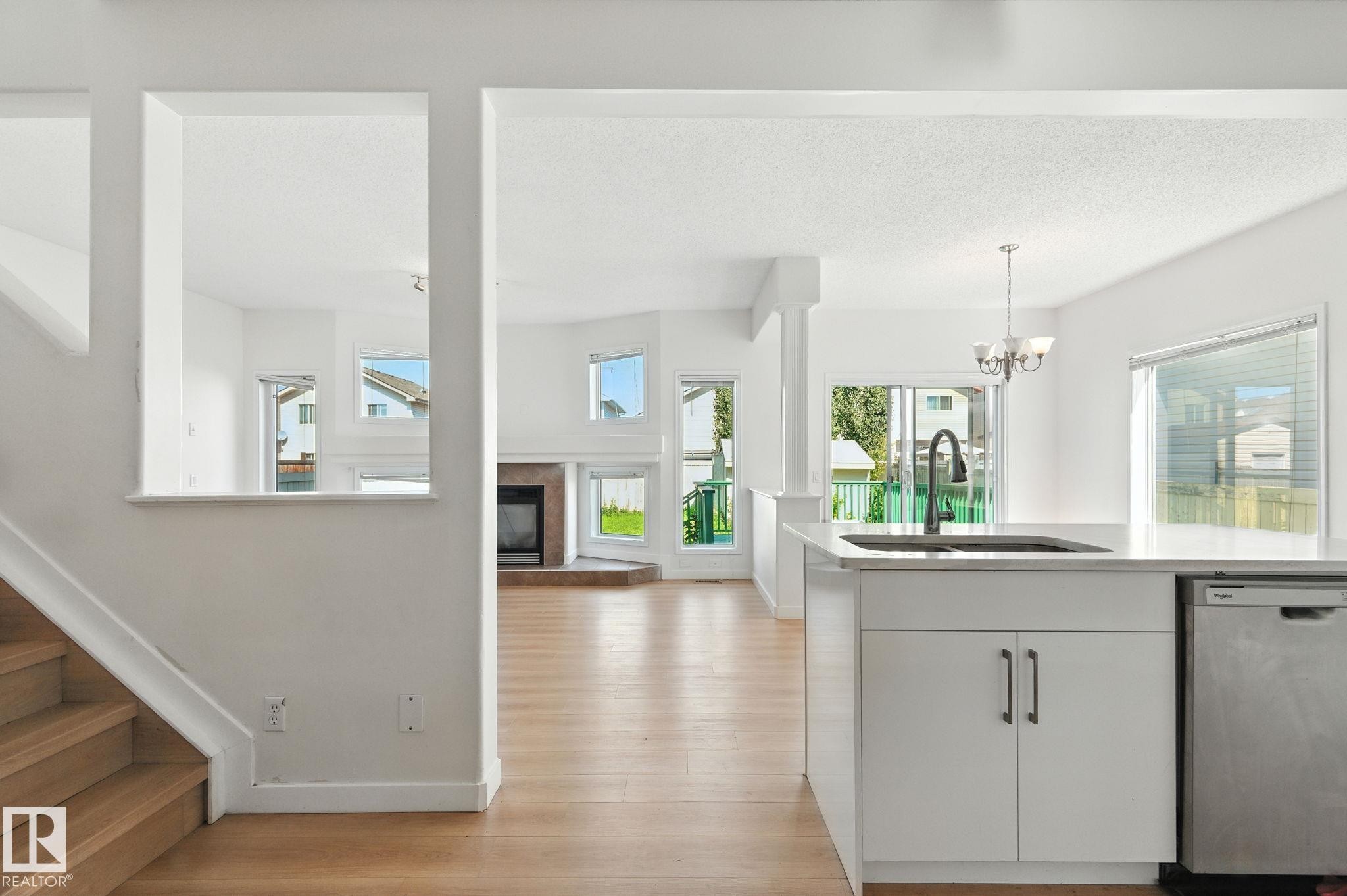 Kitchen featuring stainless steel dishwasher, decorative light fixtures, white cabinets, a tile fireplace, and a chandelier - 7836 7 Avenue, Edmonton, AB - Indoor Photo Showing Other Room
