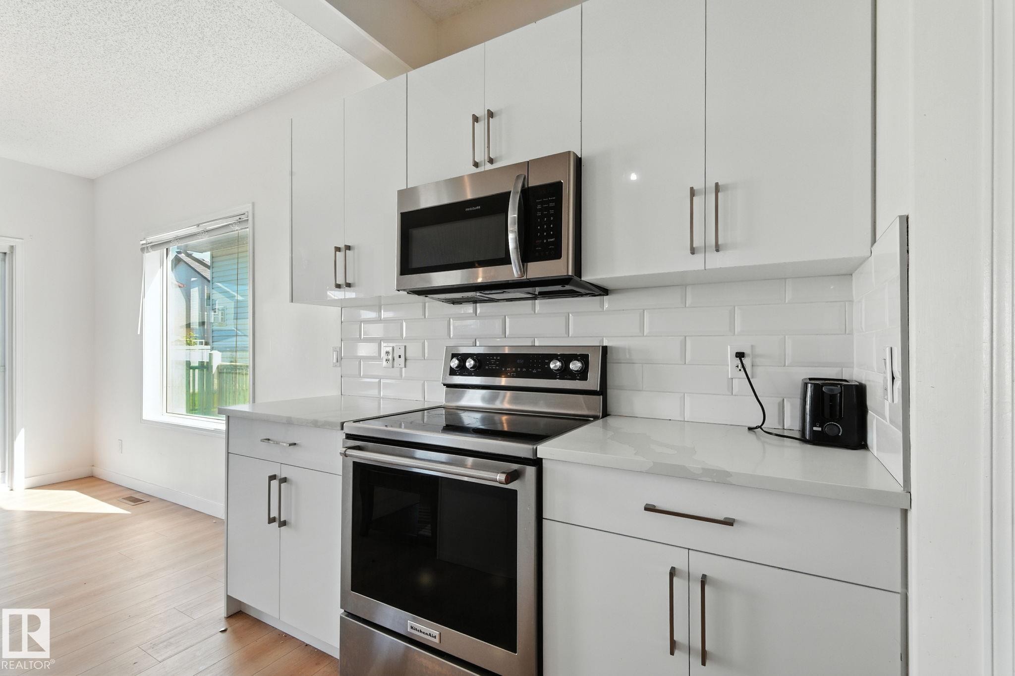 Kitchen with stainless steel appliances, white cabinetry, decorative backsplash, light stone countertops, and a textured ceiling - 7836 7 Avenue, Edmonton, AB - Indoor Photo Showing Kitchen