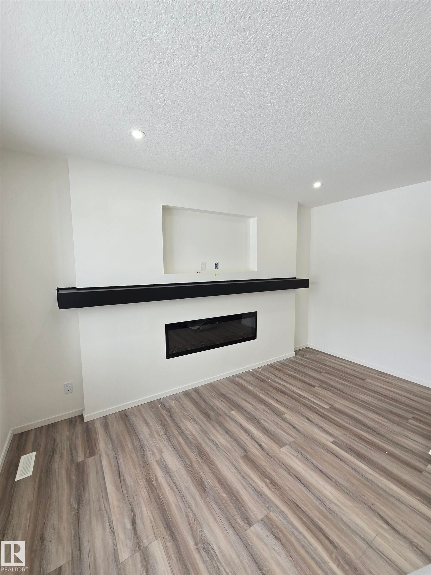 Bar with light wood finished floors, a glass covered fireplace, a textured ceiling, recessed lighting, and dark countertops - 7706 174A Avenue, Edmonton, AB - Indoor Photo Showing Other Room