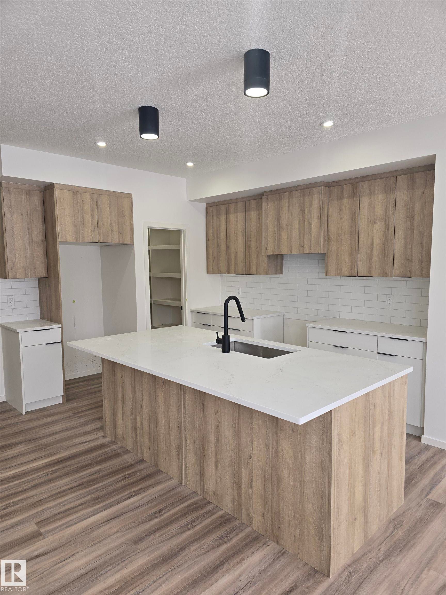 Kitchen with wood finish cabinetry, backsplash, light stone countertops, recessed lighting, and a textured ceiling - 7706 174A Avenue, Edmonton, AB - Indoor Photo Showing Kitchen