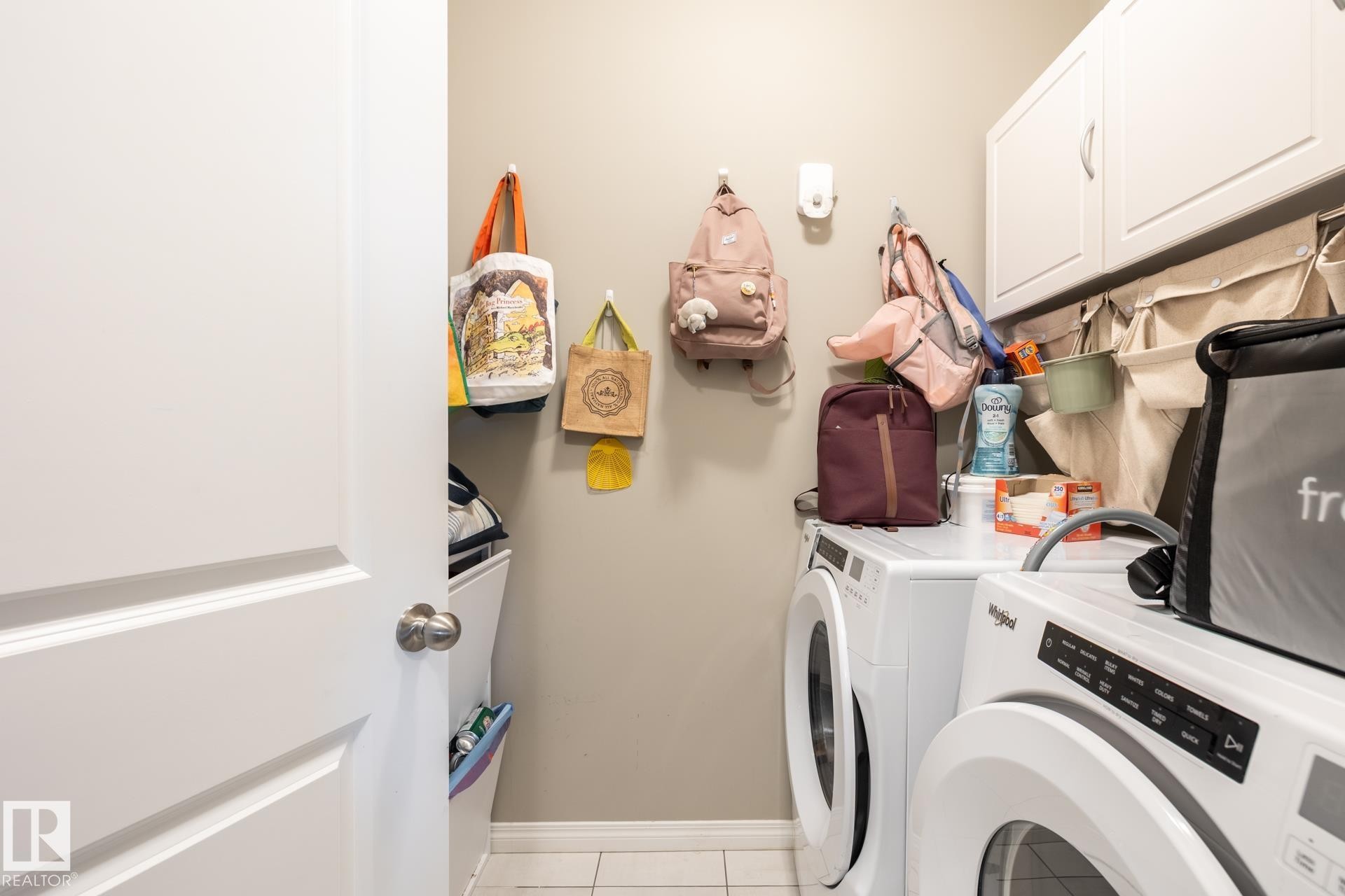 Laundry room featuring washing machine and clothes dryer, cabinet space, and light tile patterned floors - 5 2072 Wonnacott Way, Edmonton, AB - Indoor Photo Showing Laundry Room