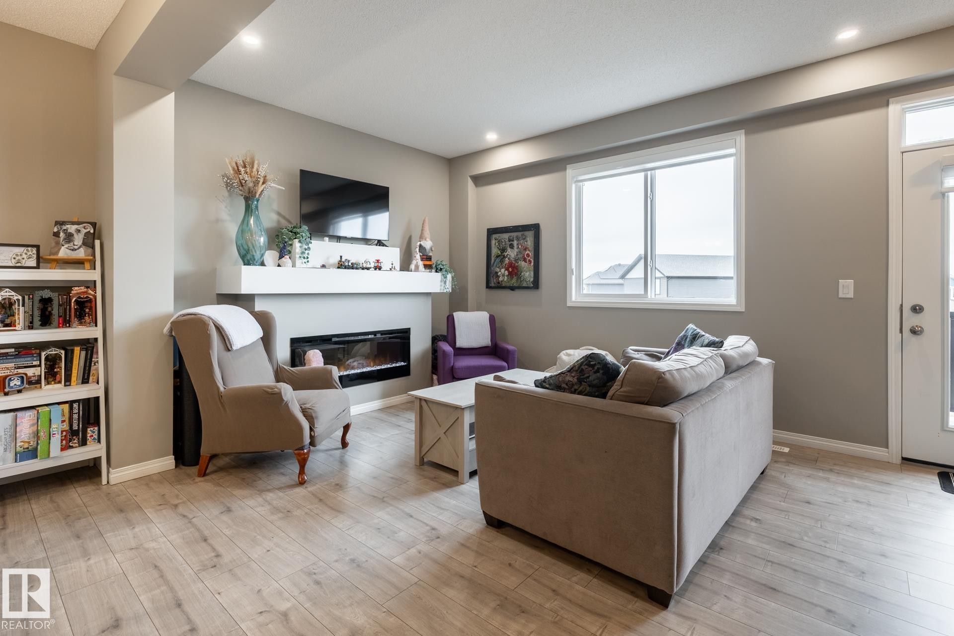 Living room with a glass covered fireplace, light wood-type flooring, and plenty of natural light - 5 2072 Wonnacott Way, Edmonton, AB - Indoor With Fireplace
