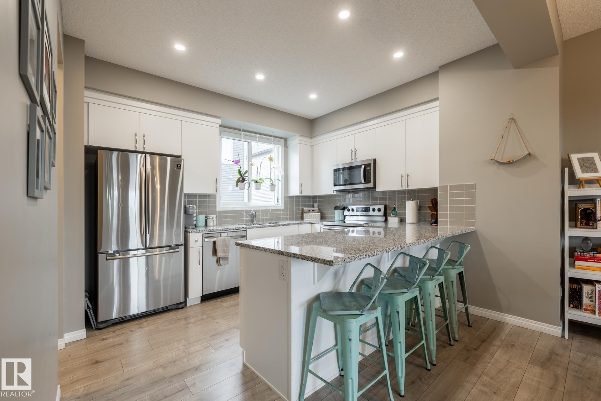 Kitchen with stainless steel appliances, a kitchen bar, a peninsula, light stone countertops, and white cabinetry - 5 2072 Wonnacott Way, Edmonton, AB - Indoor Photo Showing Kitchen With Upgraded Kitchen
