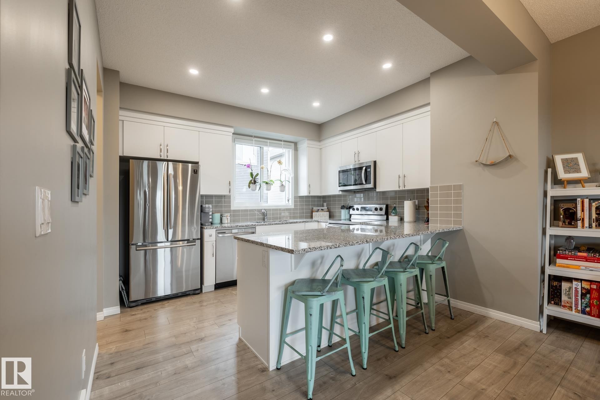 Kitchen featuring a breakfast bar, a peninsula, appliances with stainless steel finishes, light stone countertops, and white cabinetry - 5 2072 Wonnacott Way, Edmonton, AB - Indoor Photo Showing Kitchen With Upgraded Kitchen