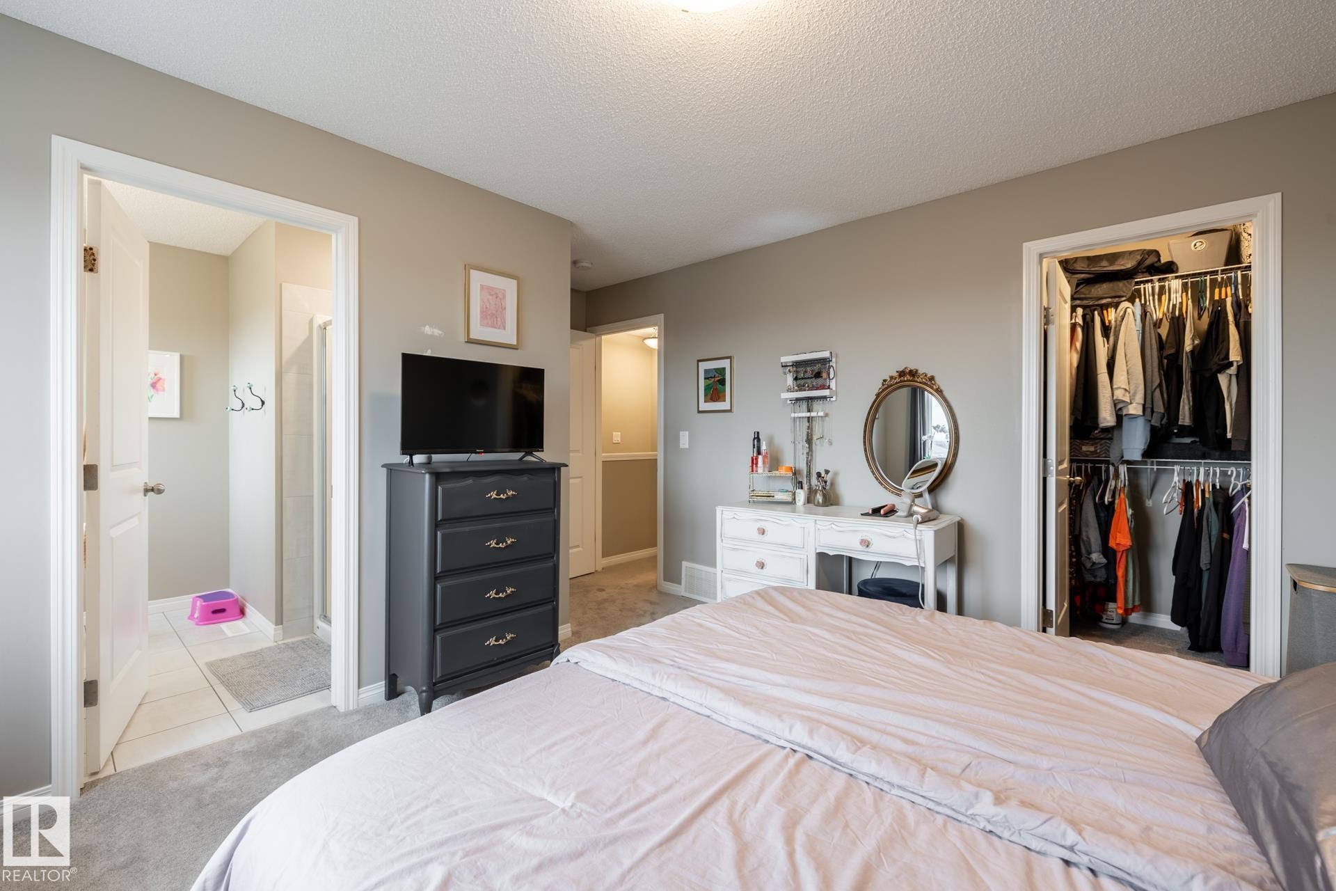 Bedroom featuring a textured ceiling, light colored carpet, a spacious closet, and ensuite bathroom - 5 2072 Wonnacott Way, Edmonton, AB - Indoor Photo Showing Bedroom