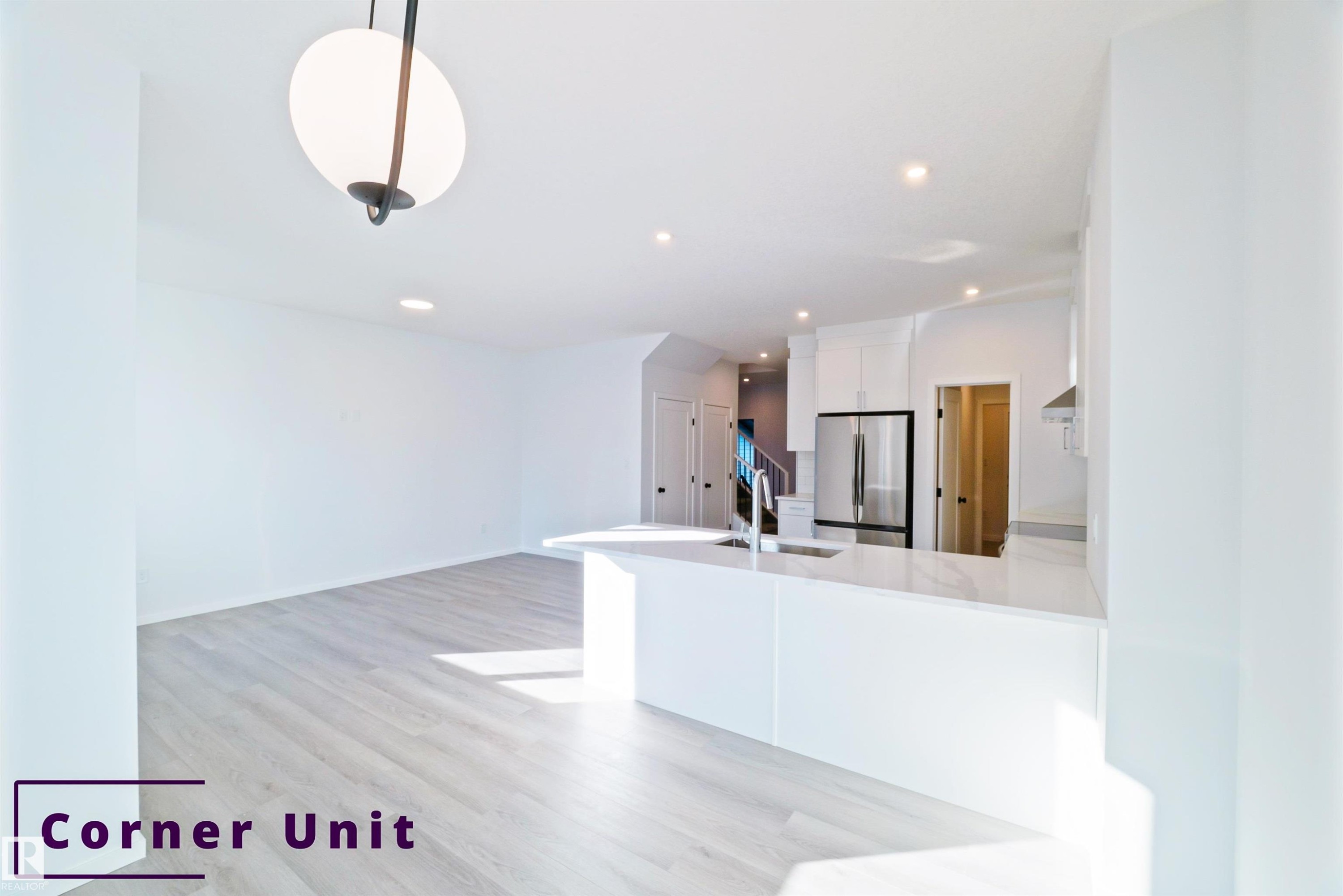 Kitchen featuring white cabinets, freestanding refrigerator, a peninsula, pendant lighting, and light wood-style flooring - 7585 174A Avenue, Edmonton, AB - Indoor Photo Showing Kitchen With Double Sink