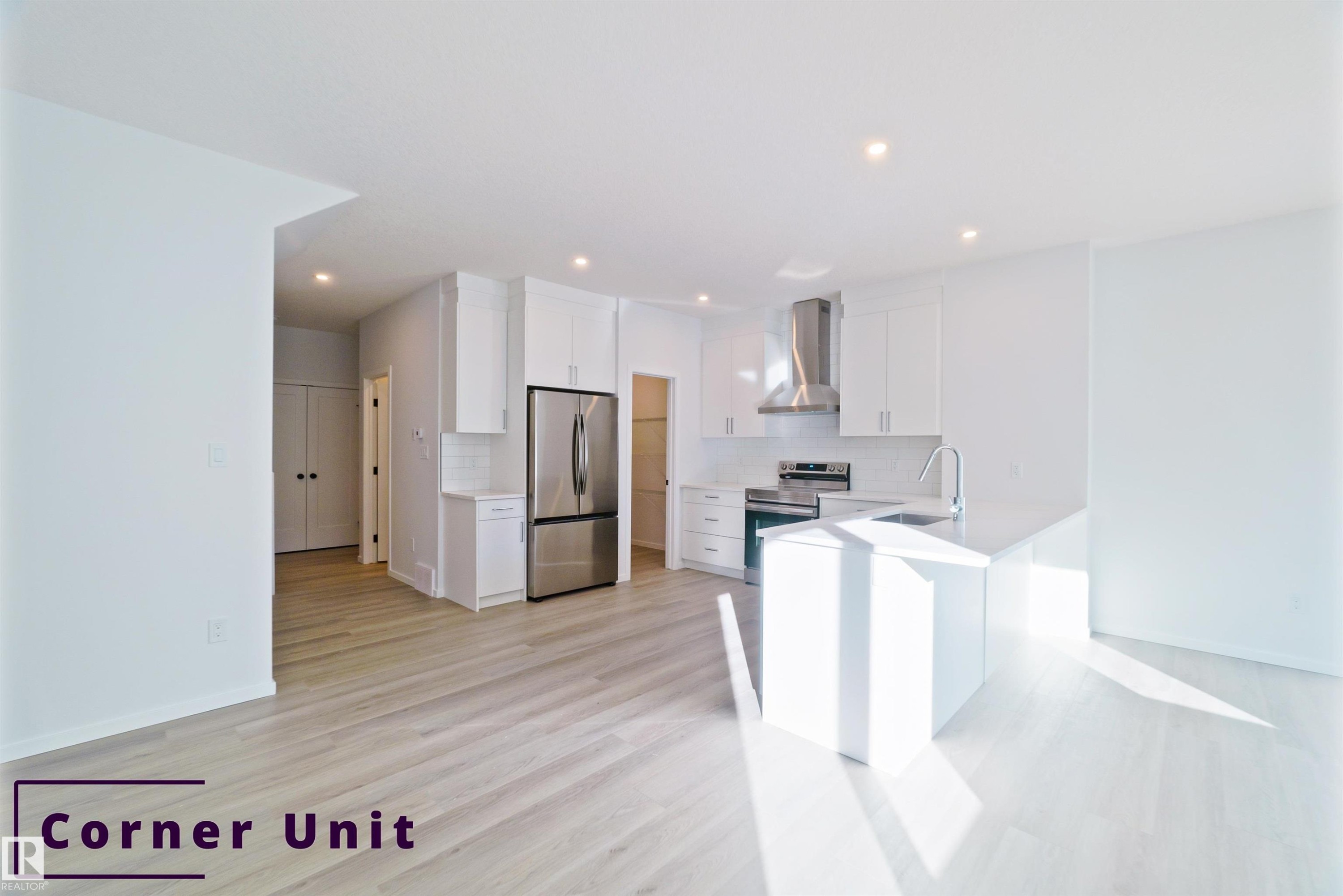 Kitchen featuring a peninsula, white cabinetry, appliances with stainless steel finishes, wall chimney range hood, and light wood finished floors - 7585 174A Avenue, Edmonton, AB - Indoor Photo Showing Kitchen
