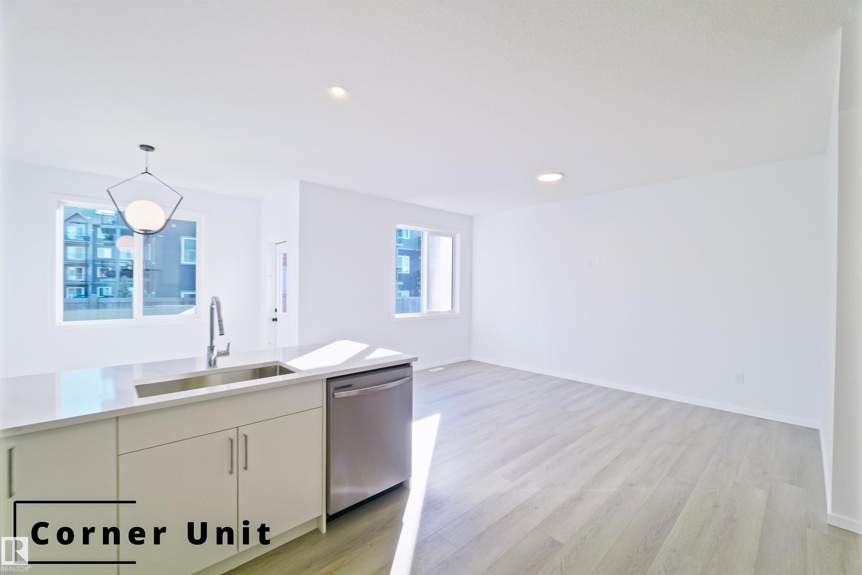 Kitchen featuring pendant lighting, stainless steel dishwasher, light wood-type flooring, white cabinetry, and open floor plan - 7585 174A Avenue, Edmonton, AB - Indoor