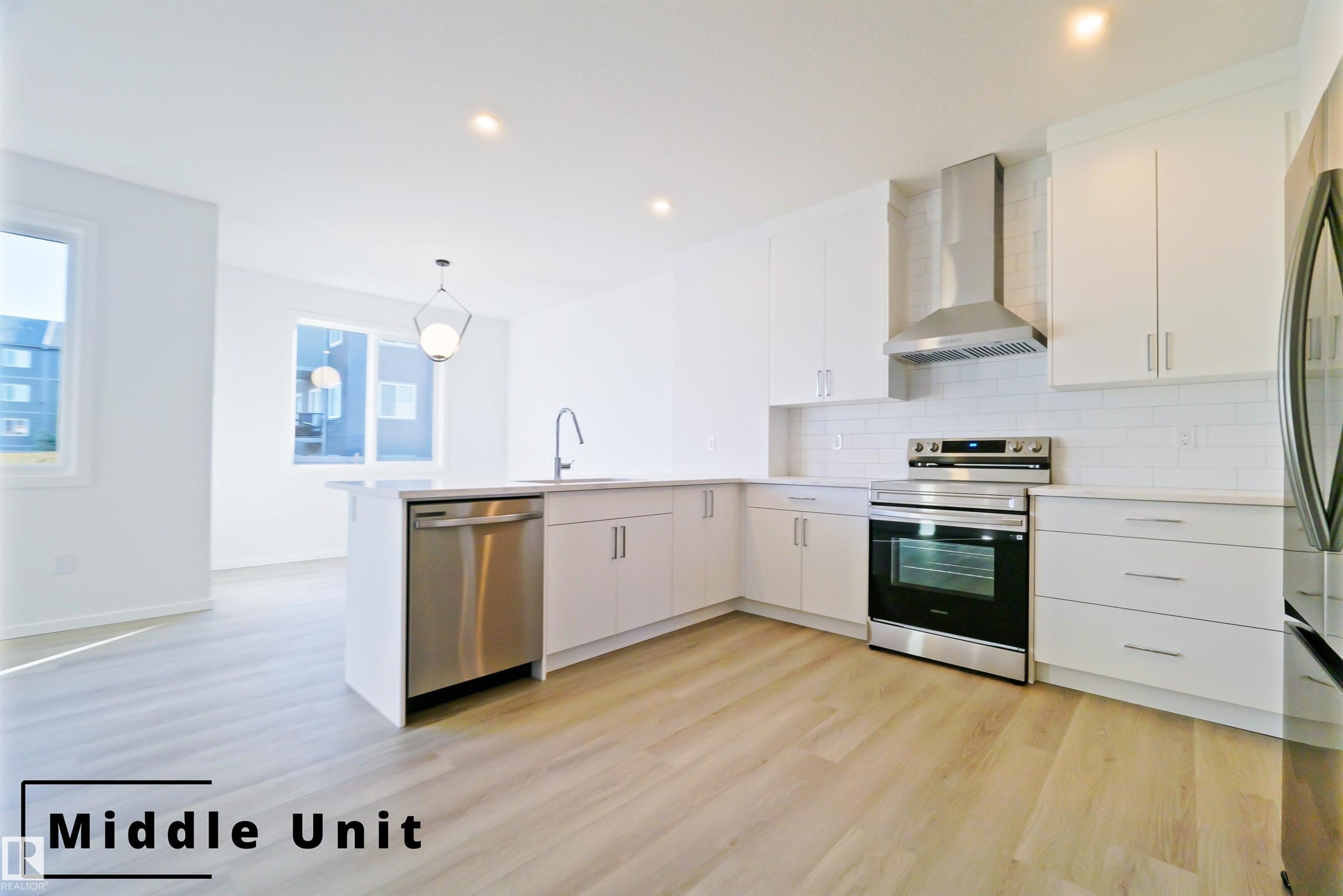 Kitchen with stainless steel appliances, white cabinets, wall chimney exhaust hood, a peninsula, and hanging light fixtures - 7585 174A Avenue, Edmonton, AB - Indoor Photo Showing Kitchen