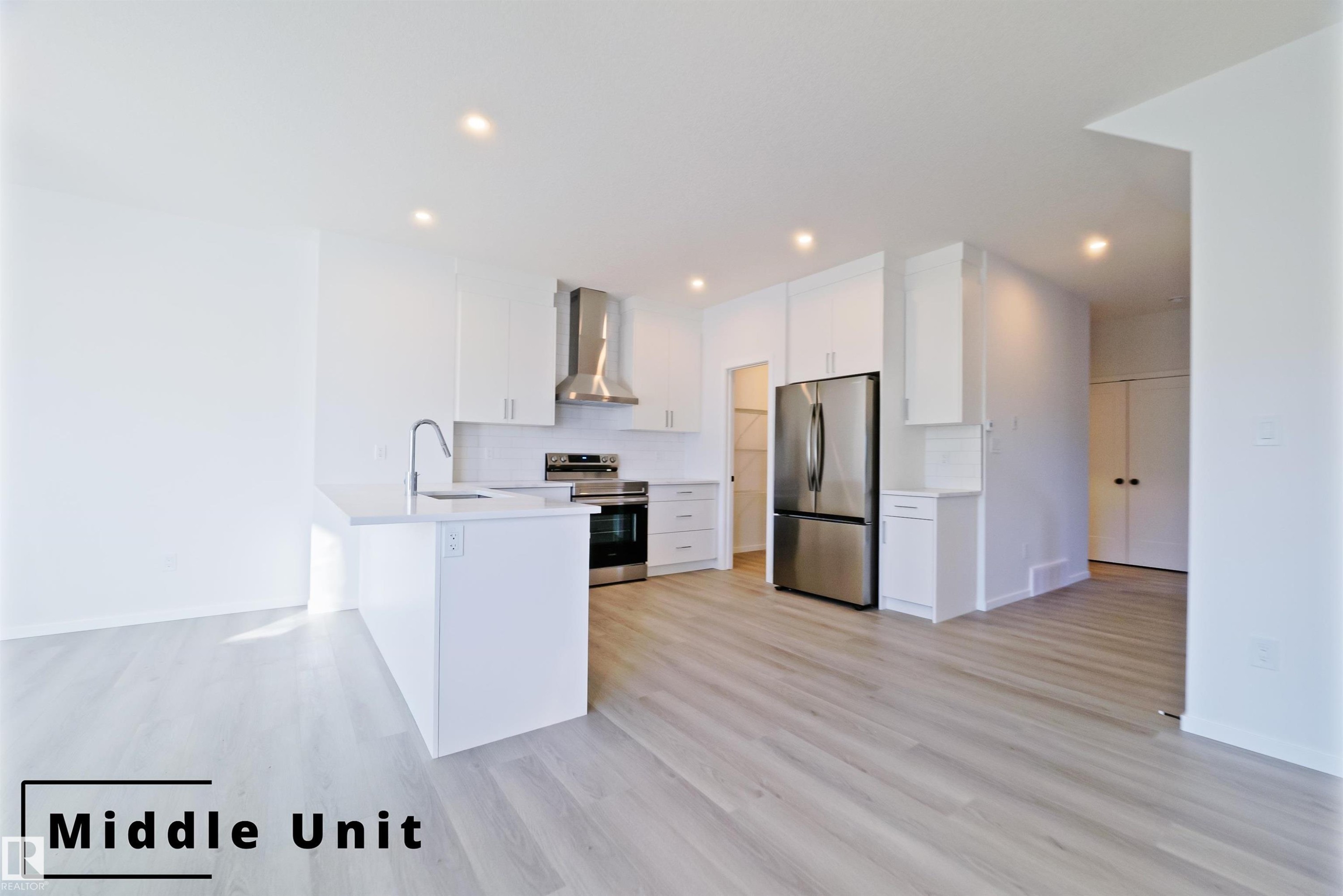 Kitchen with appliances with stainless steel finishes, white cabinetry, wall chimney range hood, a peninsula, and decorative backsplash - 7585 174A Avenue, Edmonton, AB - Indoor Photo Showing Kitchen