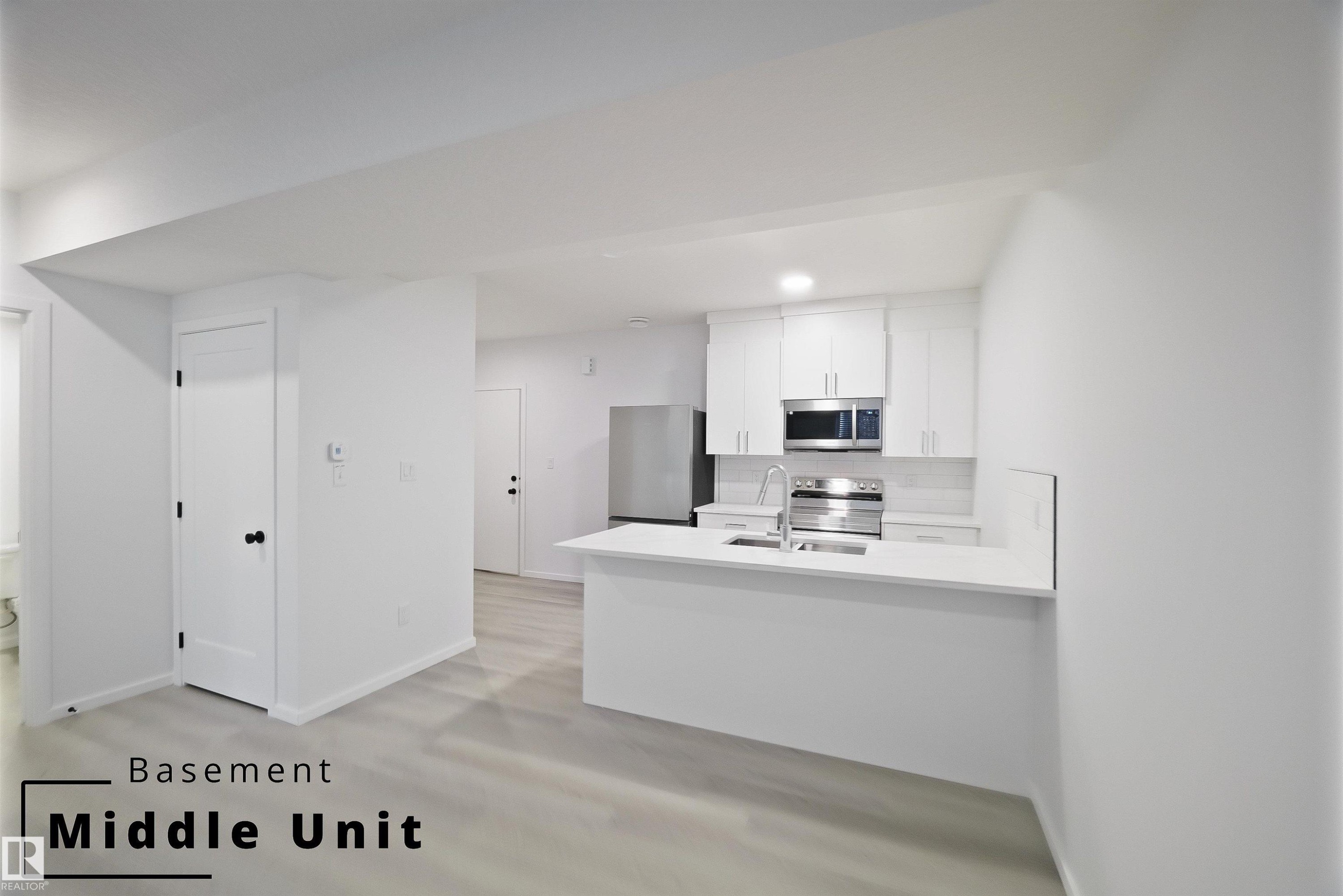 Kitchen with white cabinets, a peninsula, appliances with stainless steel finishes, decorative backsplash, and light stone countertops - 7585 174A Avenue, Edmonton, AB - Indoor Photo Showing Kitchen