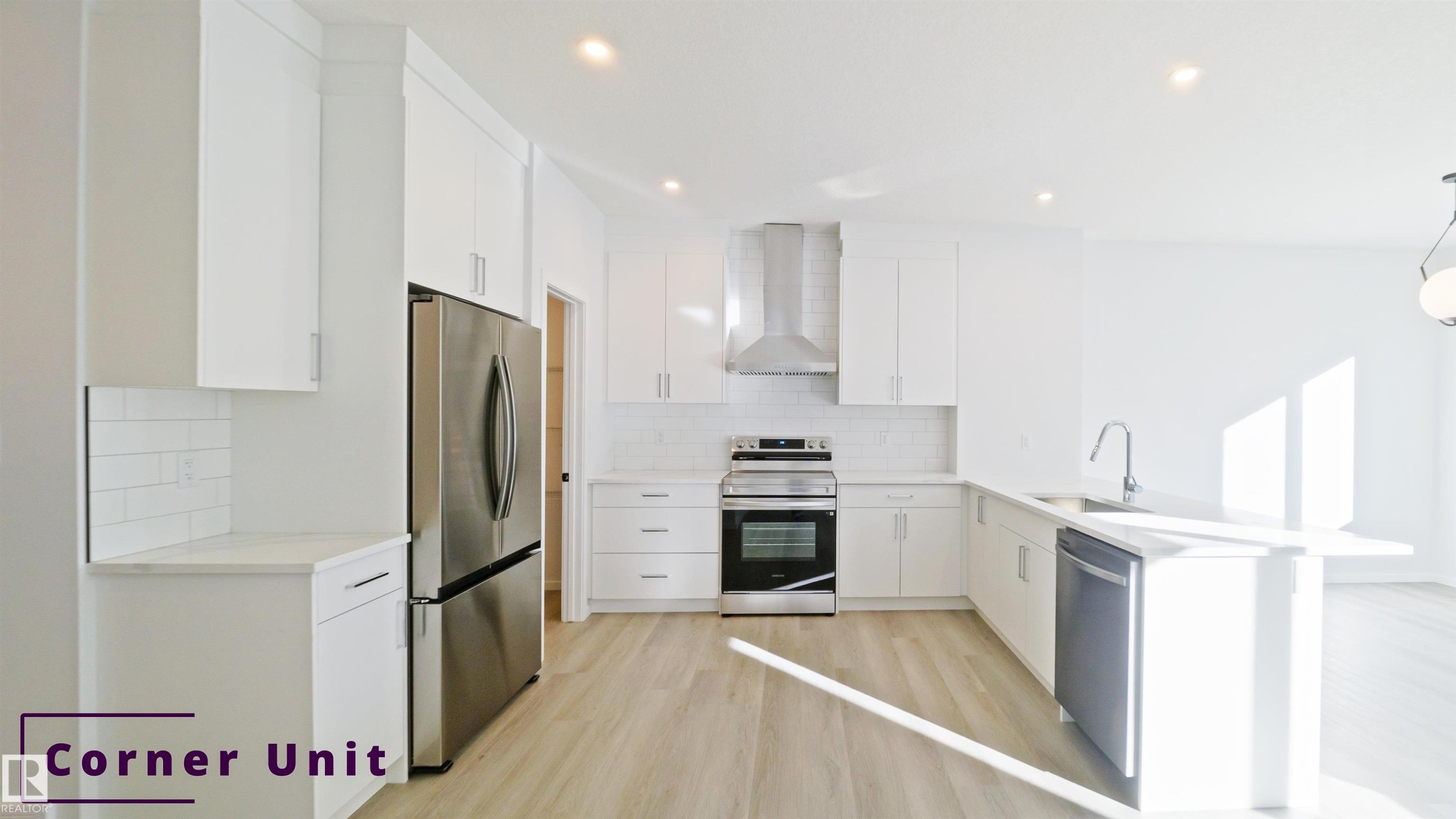 Kitchen featuring stainless steel appliances, a peninsula, white cabinetry, wall chimney exhaust hood, and decorative light fixtures - 7585 174A Avenue, Edmonton, AB - Indoor Photo Showing Kitchen With Upgraded Kitchen
