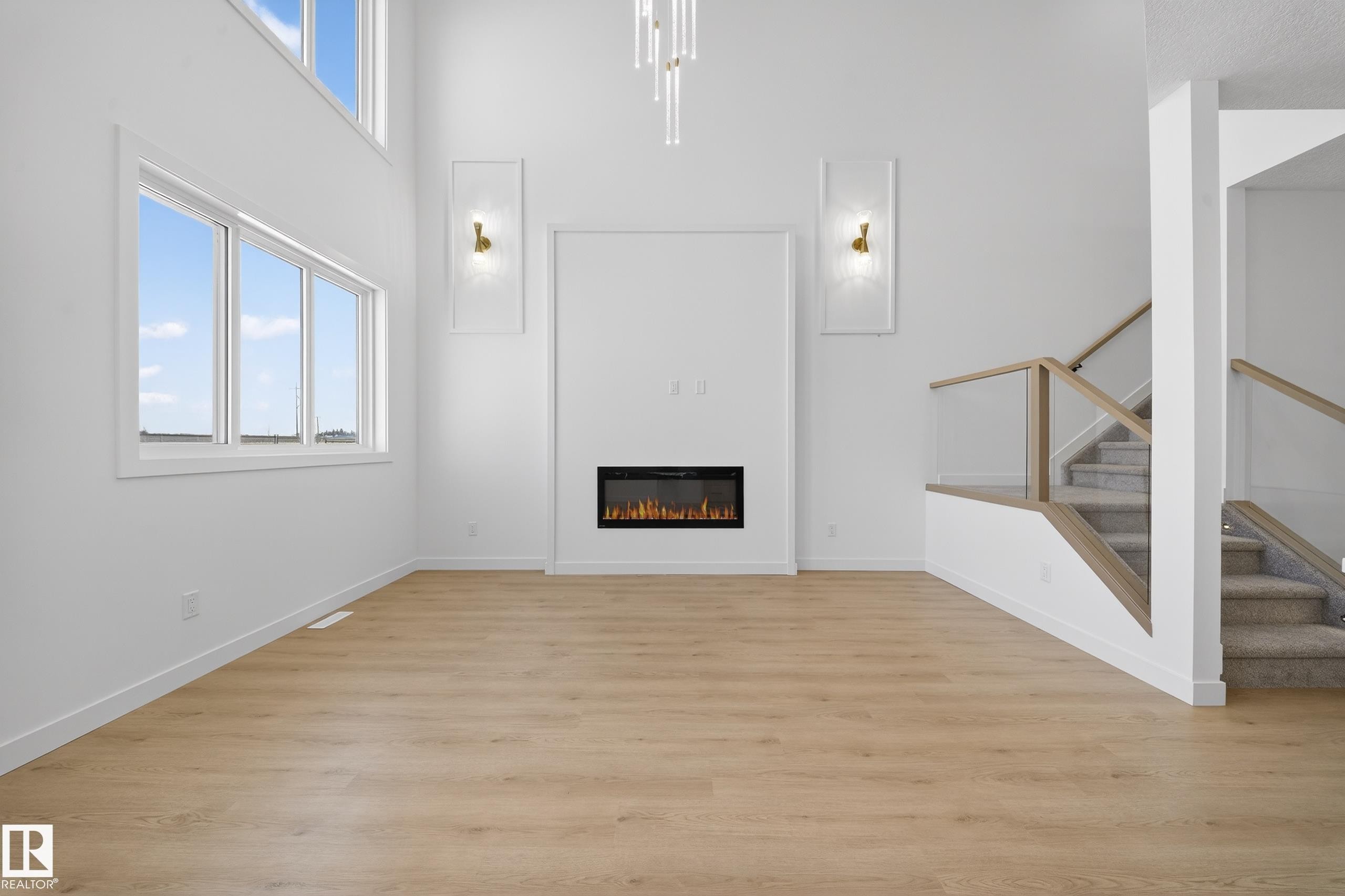 Unfurnished living room featuring plenty of natural light, light wood finished floors, a glass covered fireplace, and a high ceiling - 129 Pierwyck Loop, Spruce Grove, AB - Indoor With Fireplace