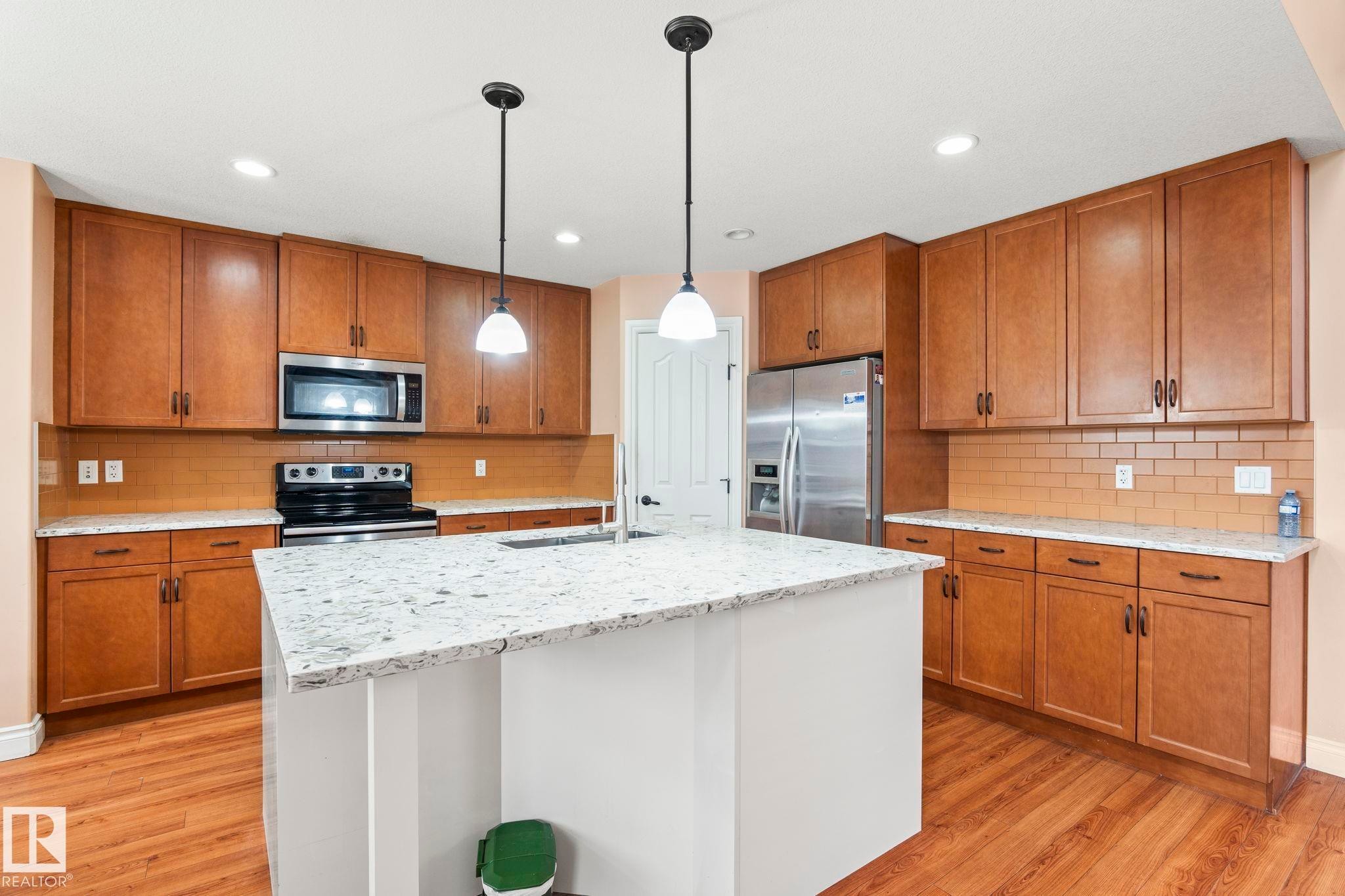 Kitchen with brown cabinets, pendant lighting, and stainless steel appliances - 1888 33 Street, Edmonton, AB - Indoor Photo Showing Kitchen
