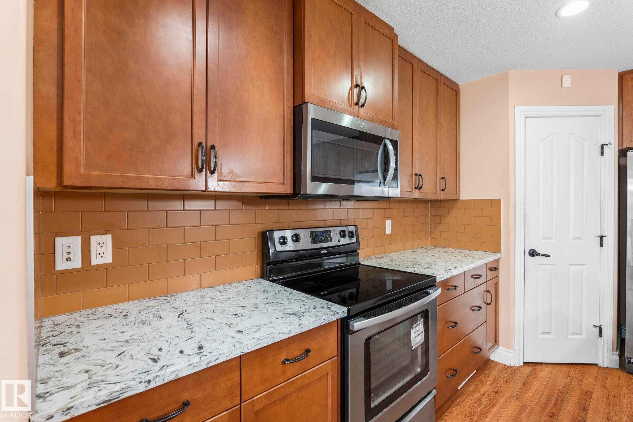 Kitchen with stainless steel appliances, brown cabinetry, light stone counters, light wood-style floors, and tasteful backsplash - 1888 33 Street, Edmonton, AB - Indoor Photo Showing Kitchen