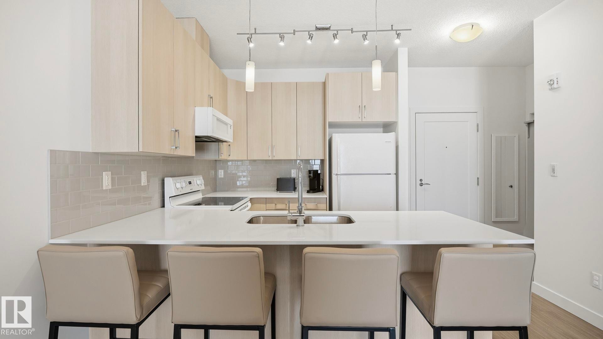 Kitchen with light brown cabinets, white appliances, tasteful backsplash, a peninsula, and a breakfast bar area - 401 17 Columbia Avenue W, Devon, AB - Indoor Photo Showing Kitchen With Double Sink With Upgraded Kitchen