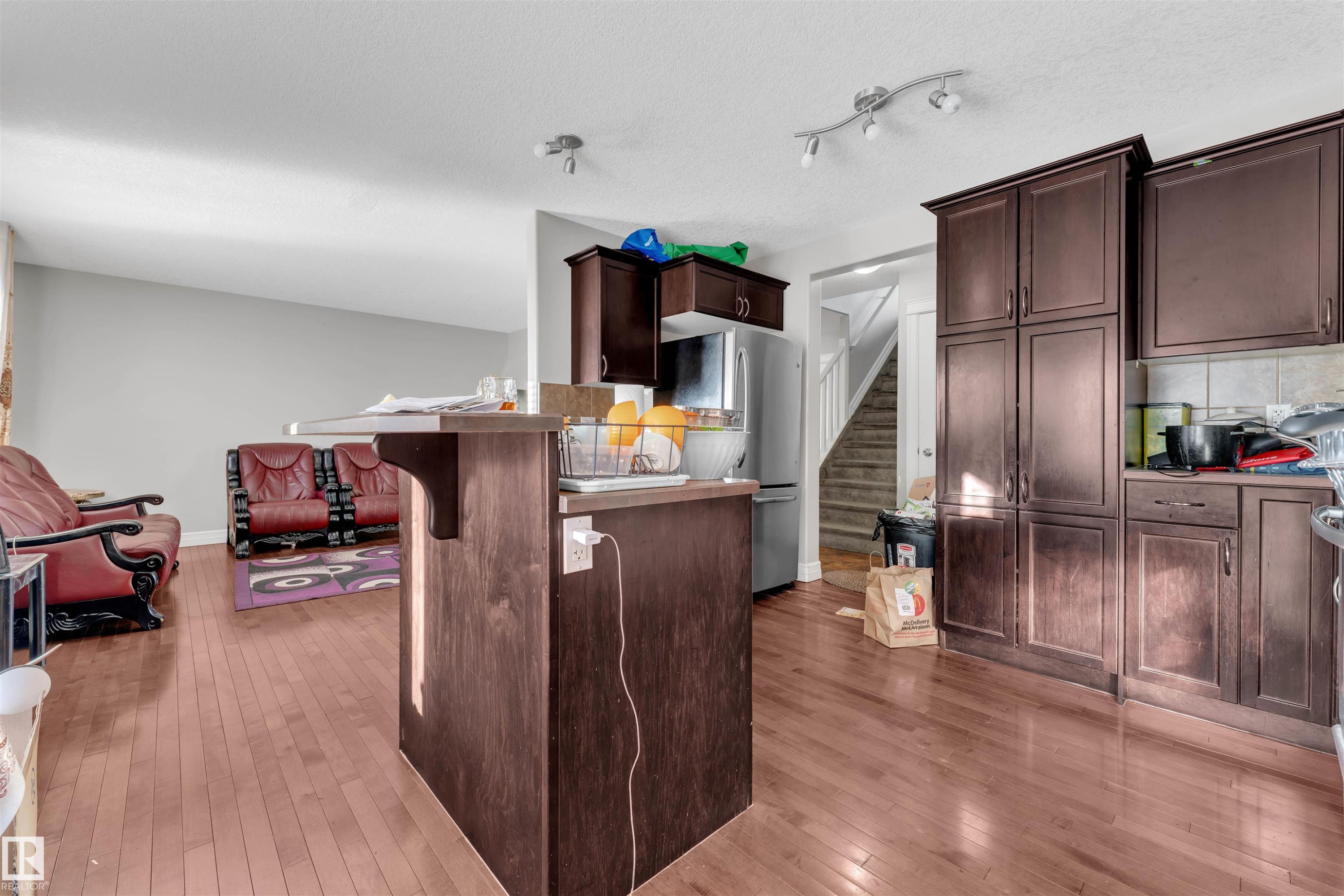 Kitchen featuring dark brown cabinets, freestanding refrigerator, a breakfast bar area, light wood-style floors, and open floor plan - 3015 26 Ave Nw, Edmonton, AB - Indoor Photo Showing Kitchen
