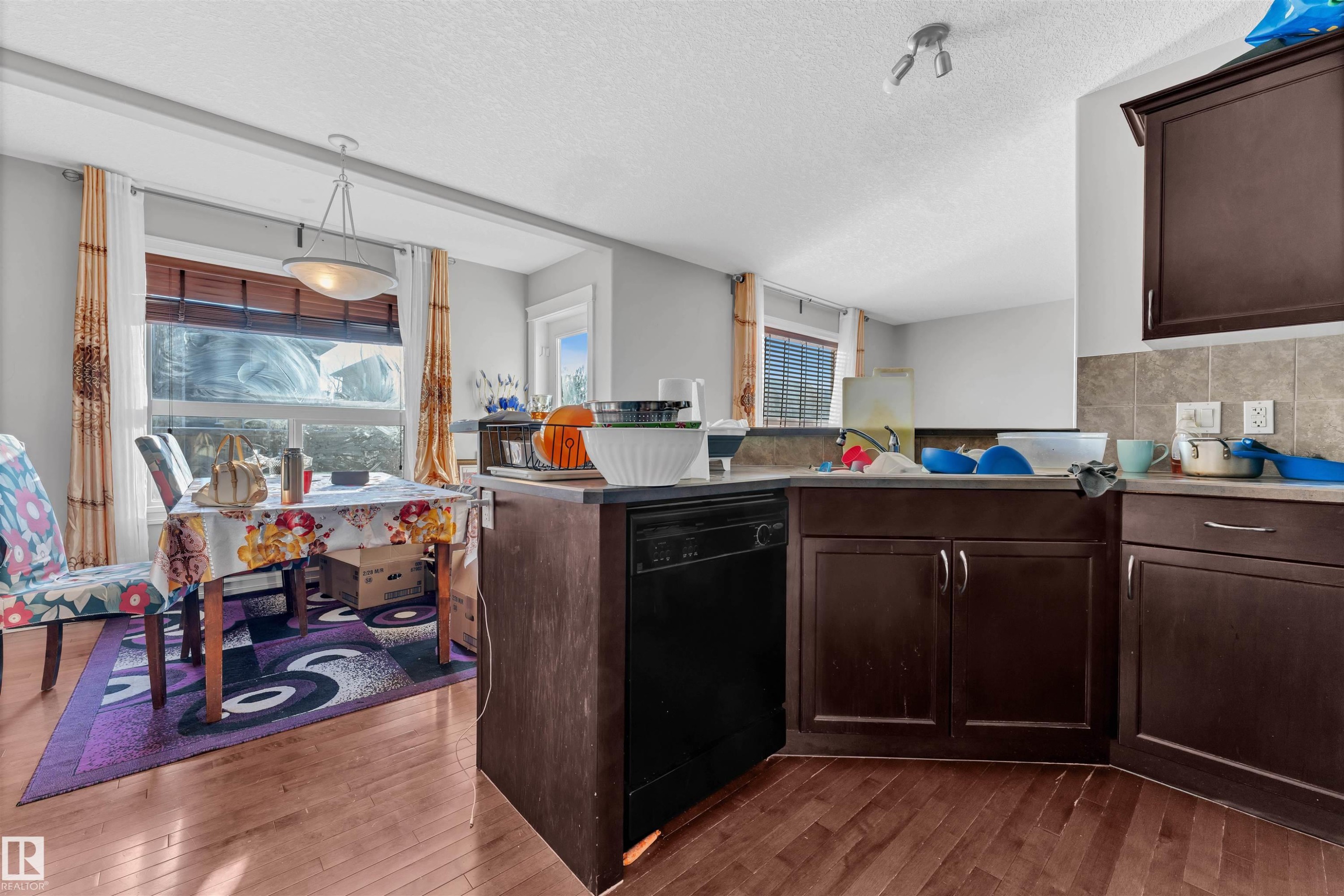 Kitchen featuring dark brown cabinetry, dishwasher, hanging light fixtures, a textured ceiling, and tasteful backsplash - 3015 26 Ave Nw, Edmonton, AB - Indoor