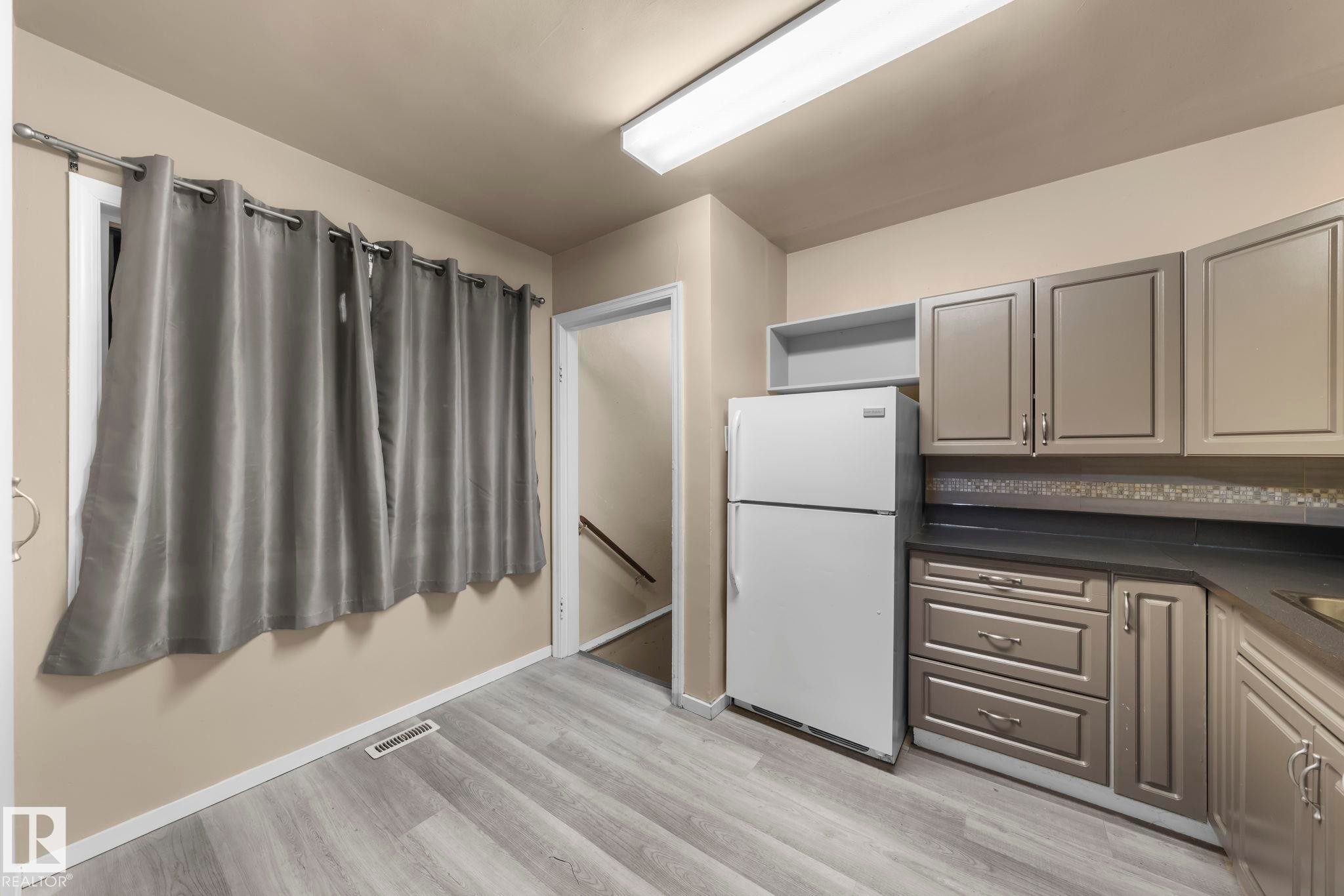Kitchen with dark countertops, freestanding refrigerator, gray cabinetry, and light wood-style floors - Edmonton, AB - Indoor Photo Showing Kitchen