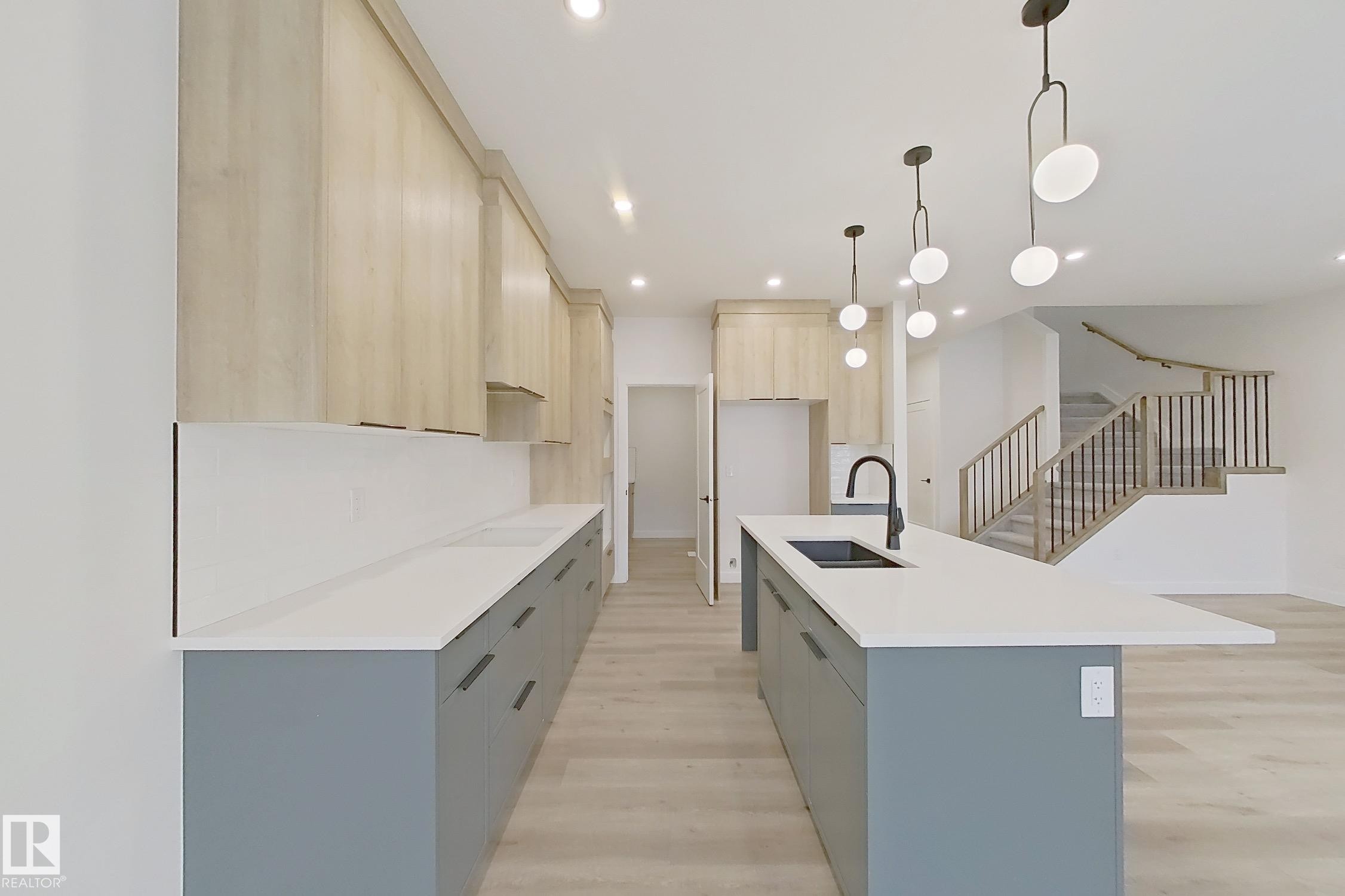Kitchen featuring modern cabinets, decorative light fixtures, light wood-type flooring, an island with sink, and recessed lighting - 3158 Magpie Way, Edmonton, AB - Indoor Photo Showing Kitchen With Double Sink With Upgraded Kitchen