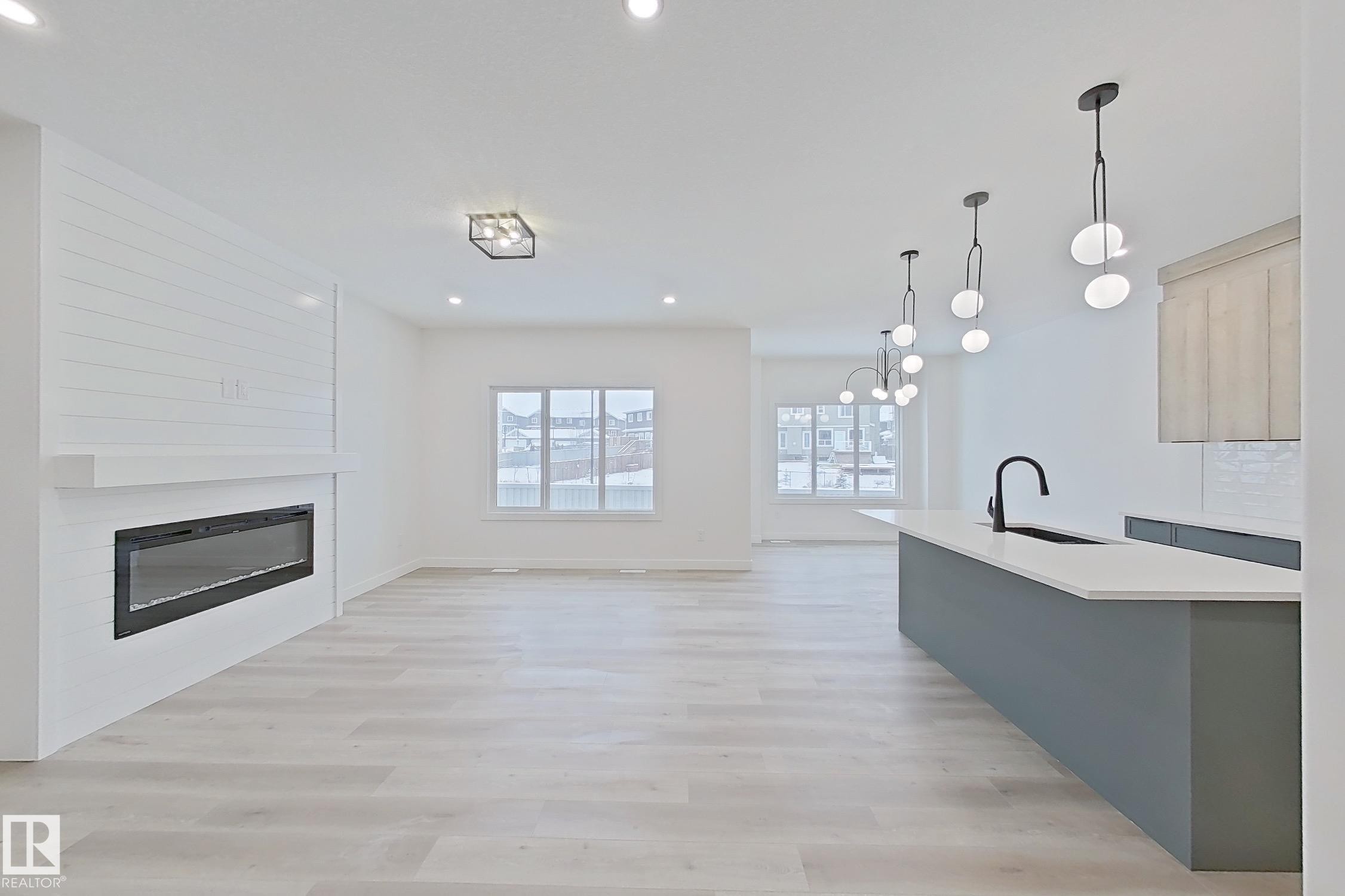 Kitchen featuring pendant lighting, light wood-style floors, a glass covered fireplace, open floor plan, and recessed lighting - 3158 Magpie Way, Edmonton, AB - Indoor With Fireplace