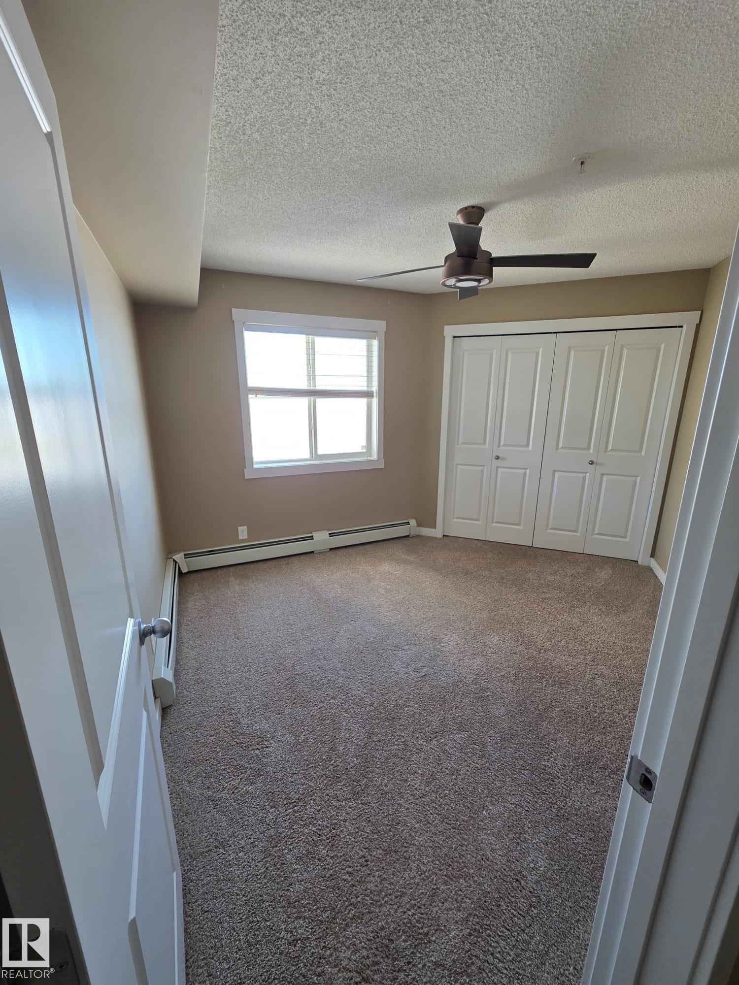 Unfurnished bedroom with carpet, a ceiling fan, a textured ceiling, a closet, and a baseboard heating unit - 313 1510 Watt Drive, Edmonton, AB - Indoor Photo Showing Other Room