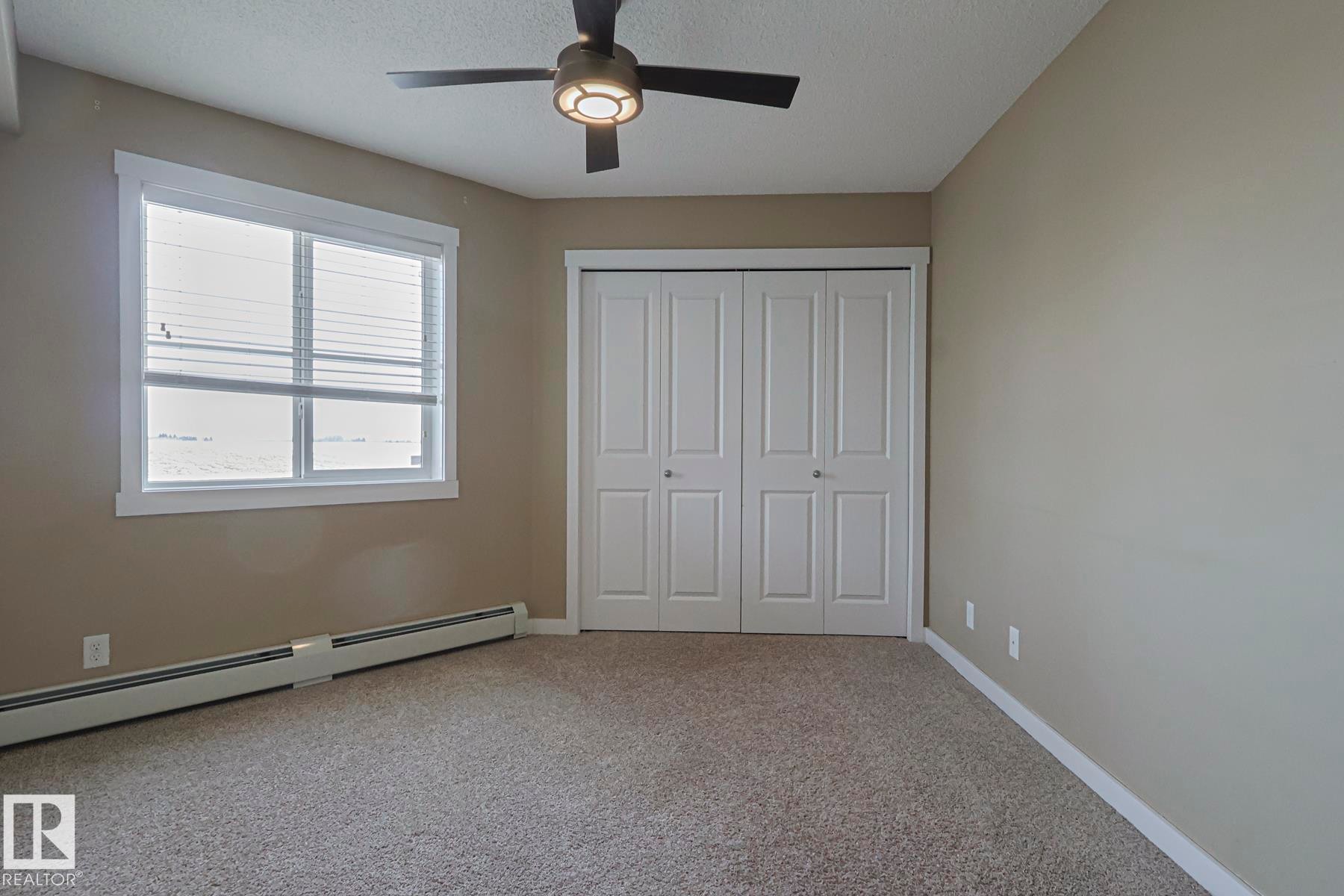 Unfurnished bedroom with light colored carpet, ceiling fan, a closet, baseboard heating, and a textured ceiling - 313 1510 Watt Drive, Edmonton, AB - Indoor Photo Showing Other Room