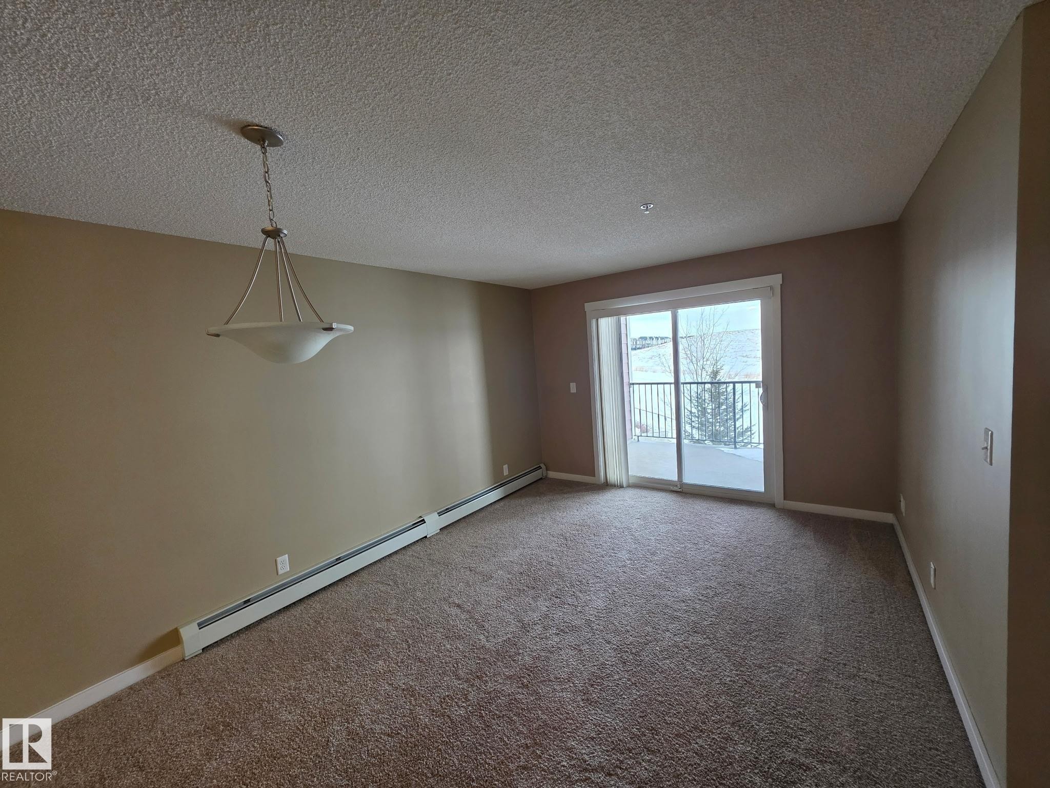Carpeted empty room featuring a baseboard radiator and a textured ceiling - 313 1510 Watt Drive, Edmonton, AB - Indoor Photo Showing Other Room