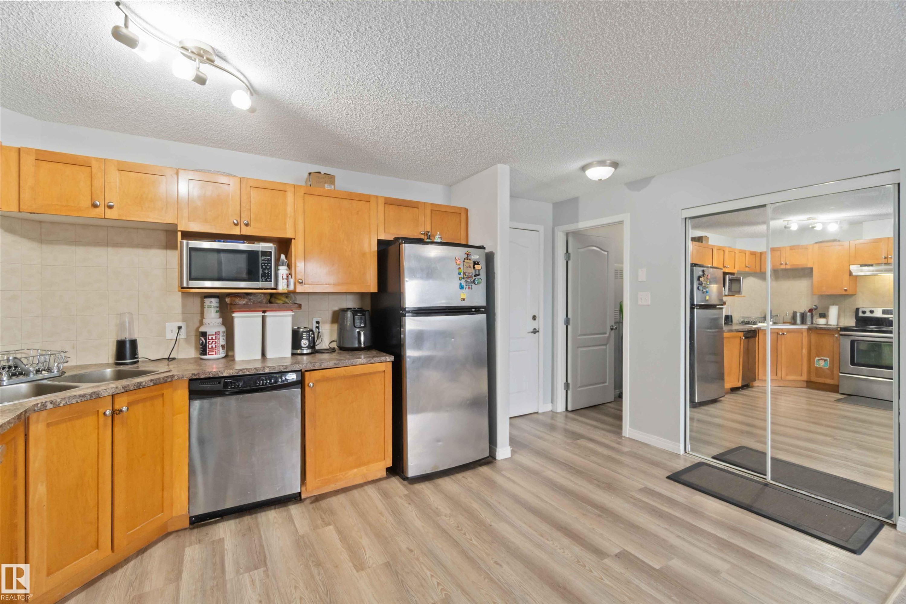 Kitchen with tasteful backsplash, stainless steel appliances, a textured ceiling, light wood-type flooring, and brown cabinets - 2117 9357 Simpson Drive, Edmonton, AB - Indoor Photo Showing Kitchen With Double Sink