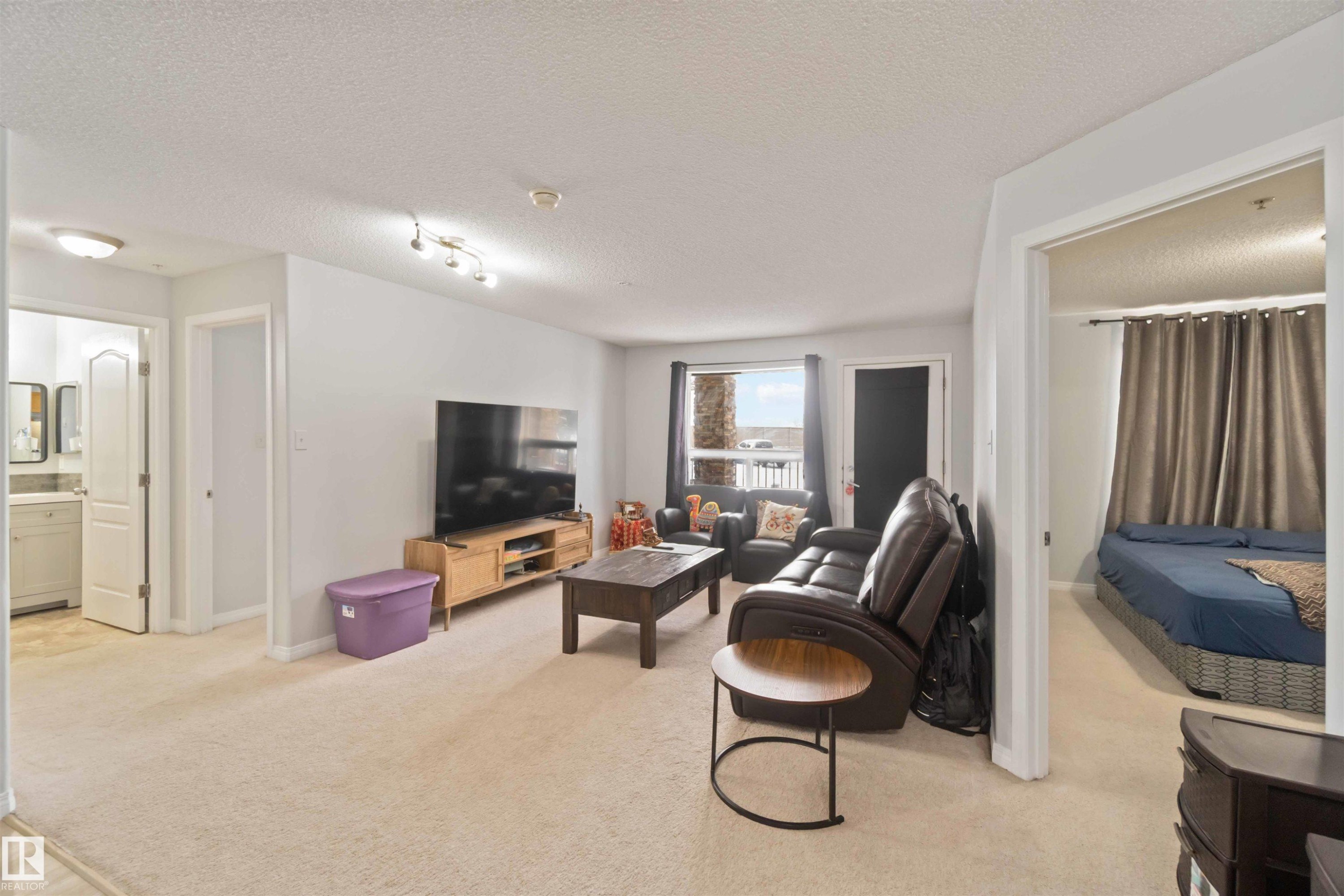 Living area featuring light colored carpet and a textured ceiling - 2117 9357 Simpson Drive, Edmonton, AB - Indoor Photo Showing Living Room