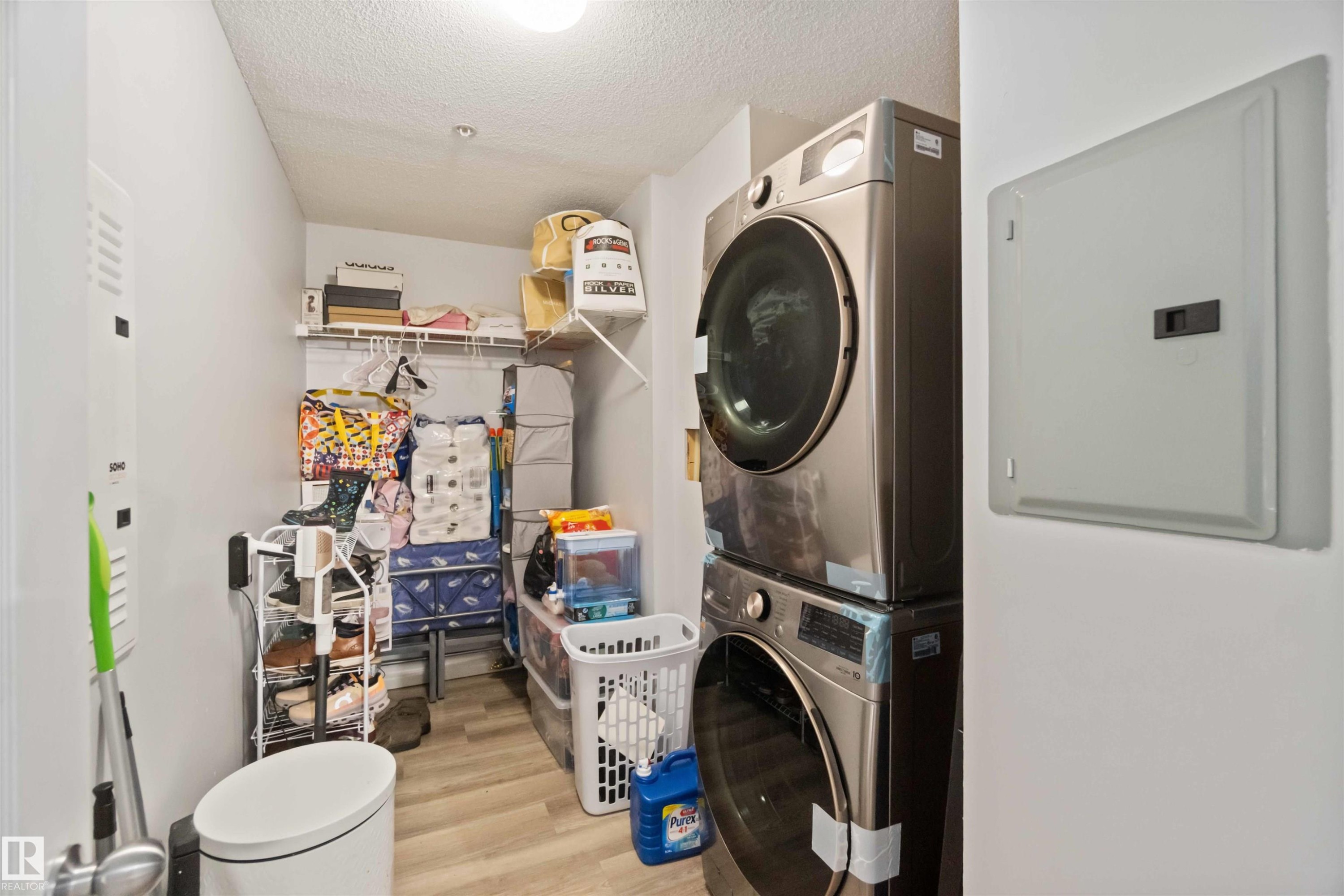 Laundry room featuring electric panel, a textured ceiling, stacked washer / dryer, and light wood-style floors - 2117 9357 Simpson Drive, Edmonton, AB - Indoor Photo Showing Laundry Room