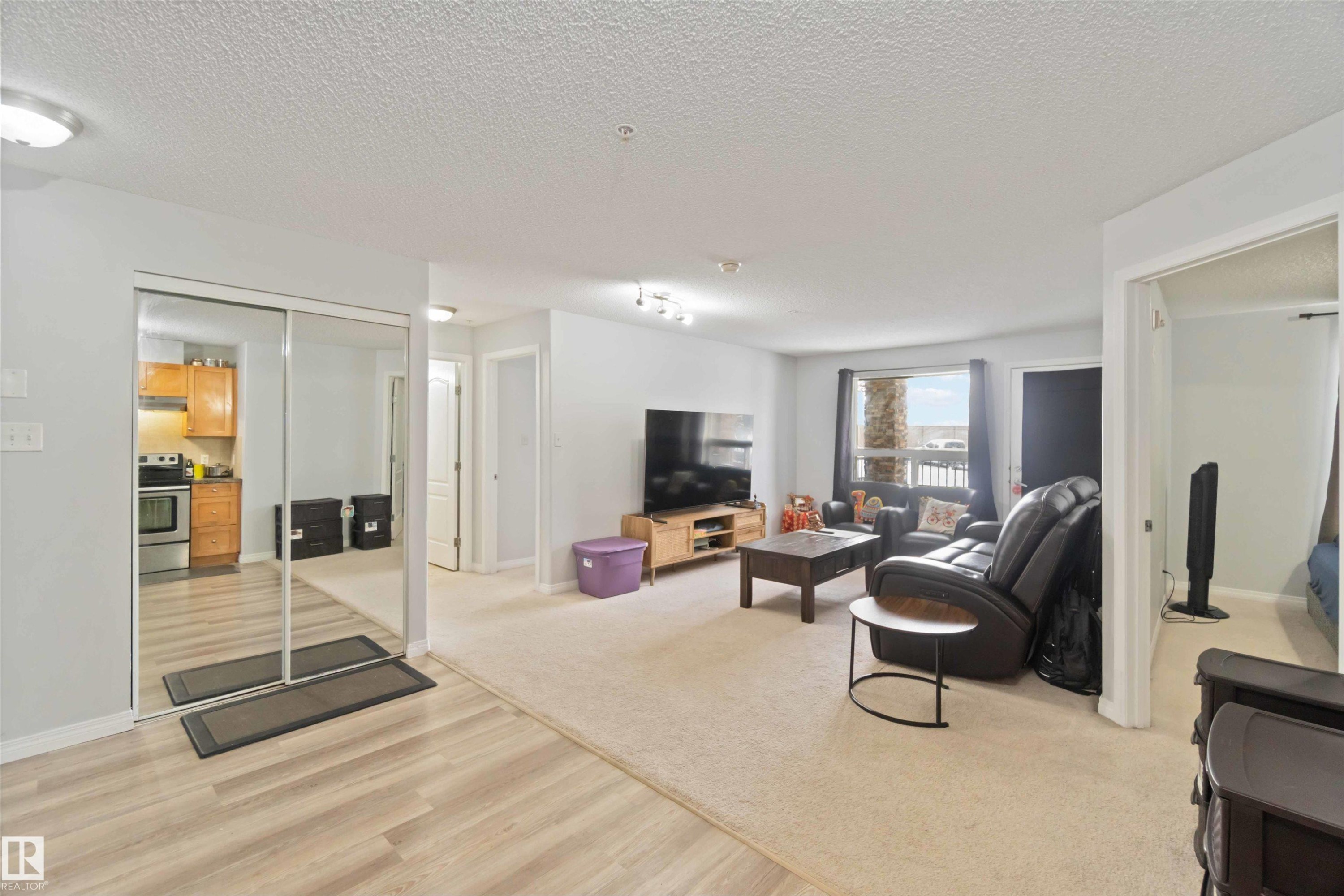 Living area featuring a textured ceiling, light wood-type flooring, and light colored carpet - 2117 9357 Simpson Drive, Edmonton, AB - Indoor