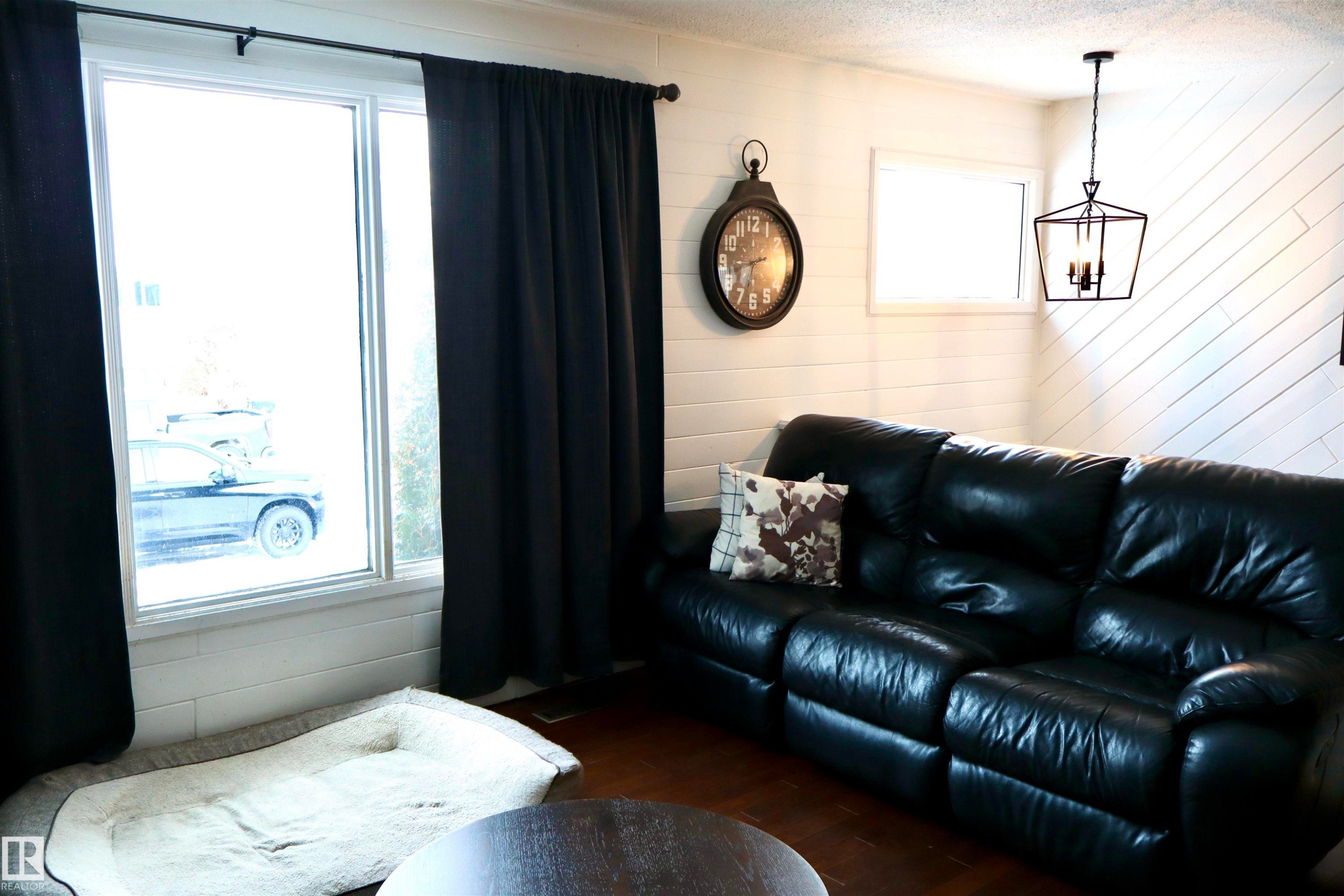 Living room with wood walls, a textured ceiling, dark wood finished floors, and a chandelier - 4505 58 Avenue, Barrhead, AB - Indoor Photo Showing Living Room