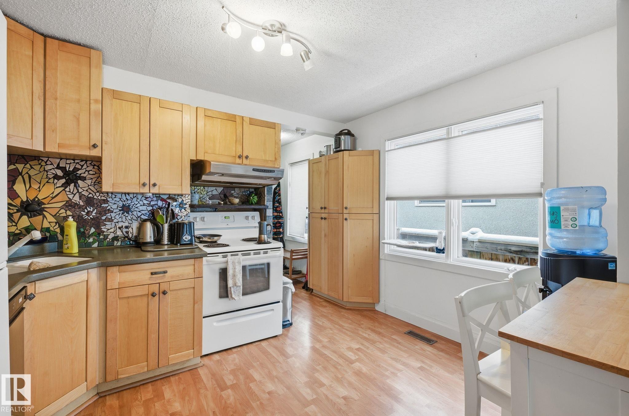 Kitchen featuring white range with electric cooktop, backsplash, under cabinet range hood, light wood-style floors, and a textured ceiling - 9705 87 Avenue, Edmonton, AB - Indoor Photo Showing Kitchen