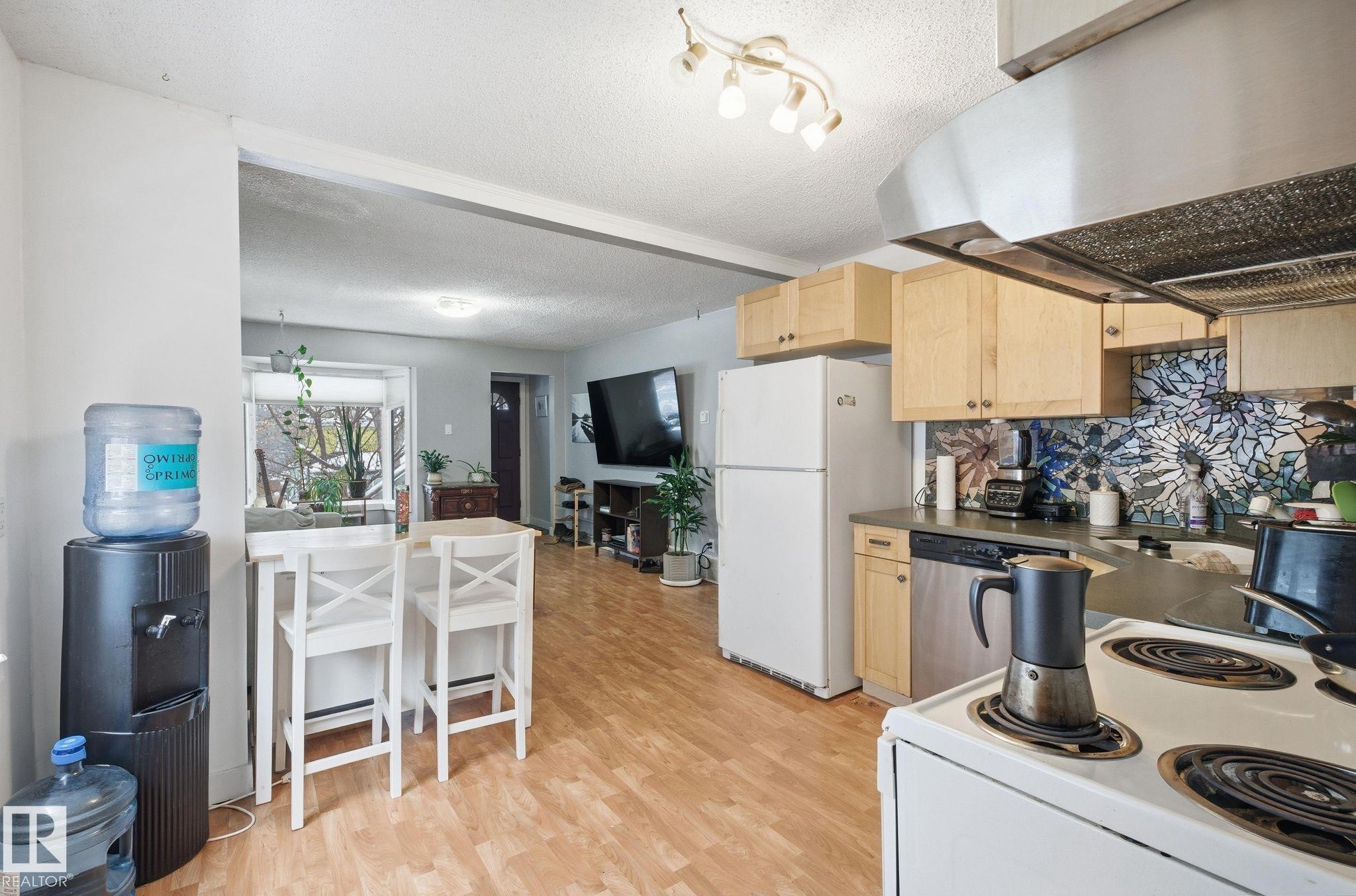 Kitchen featuring under cabinet range hood, light brown cabinetry, white appliances, a textured ceiling, and dark countertops - 9705 87 Avenue, Edmonton, AB - Indoor Photo Showing Kitchen