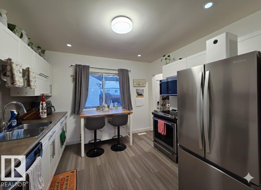 Kitchen with stainless steel appliances, white cabinetry, dark wood-type flooring, and recessed lighting - 12410 120 Avenue, Edmonton, AB - Indoor Photo Showing Kitchen With Double Sink