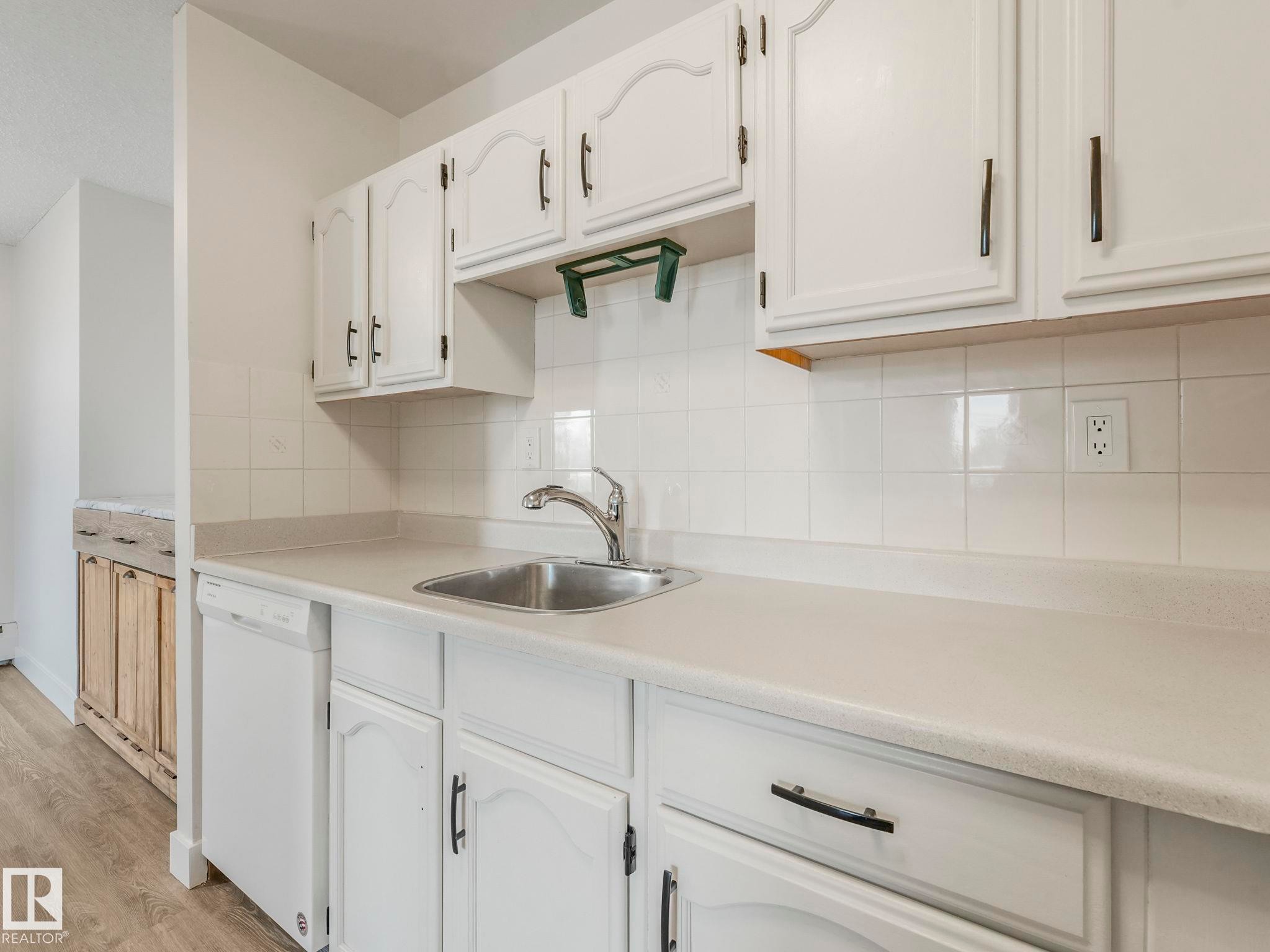 Kitchen featuring light countertops, decorative backsplash, dishwasher, white cabinetry, and light wood finished floors - 406 10125 109 Street, Edmonton, AB - Indoor Photo Showing Kitchen