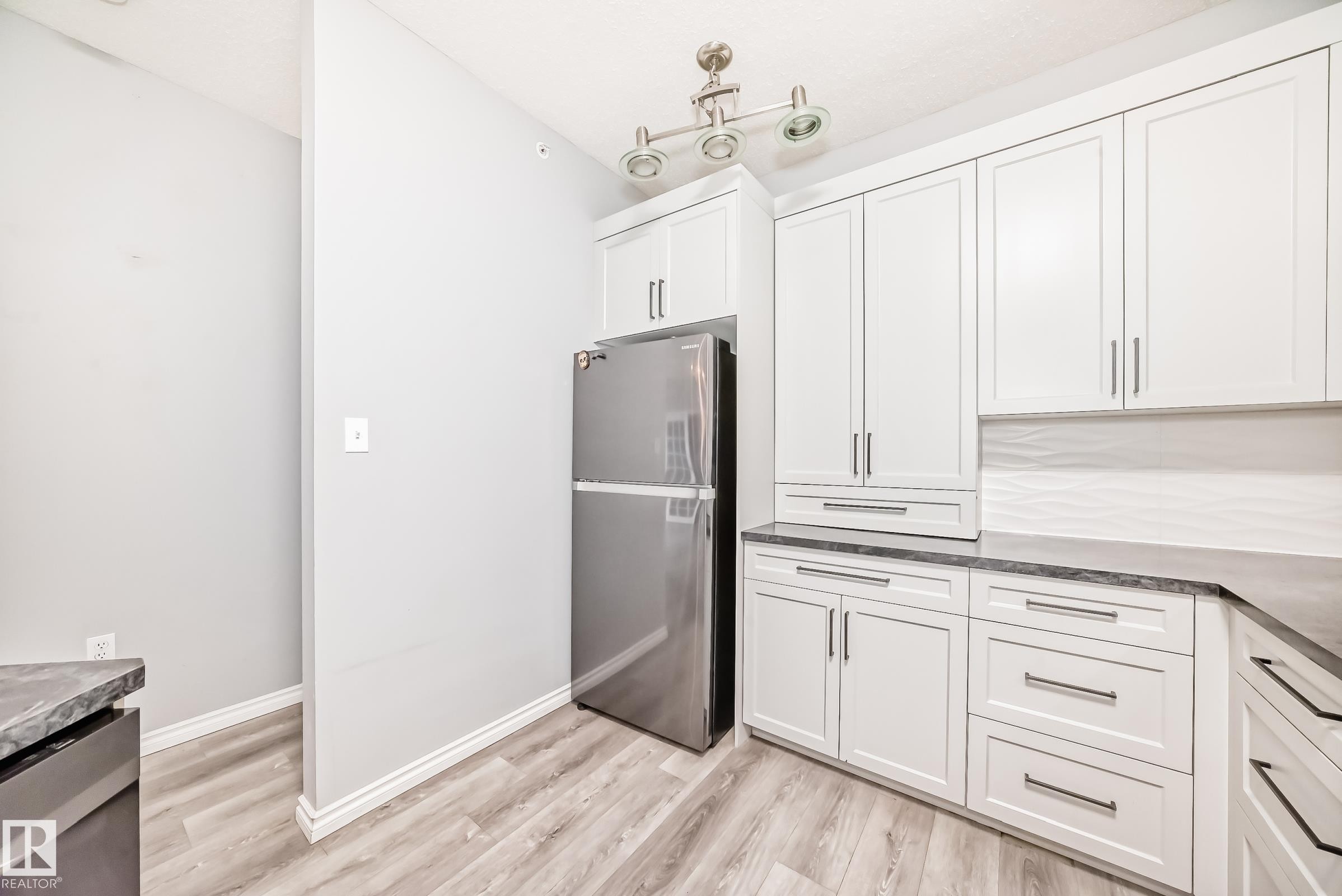 Kitchen featuring stainless steel appliances, white cabinets, light wood-type flooring, and dark stone counters - 507 11716 100 Avenue, Edmonton, AB - Indoor Photo Showing Kitchen