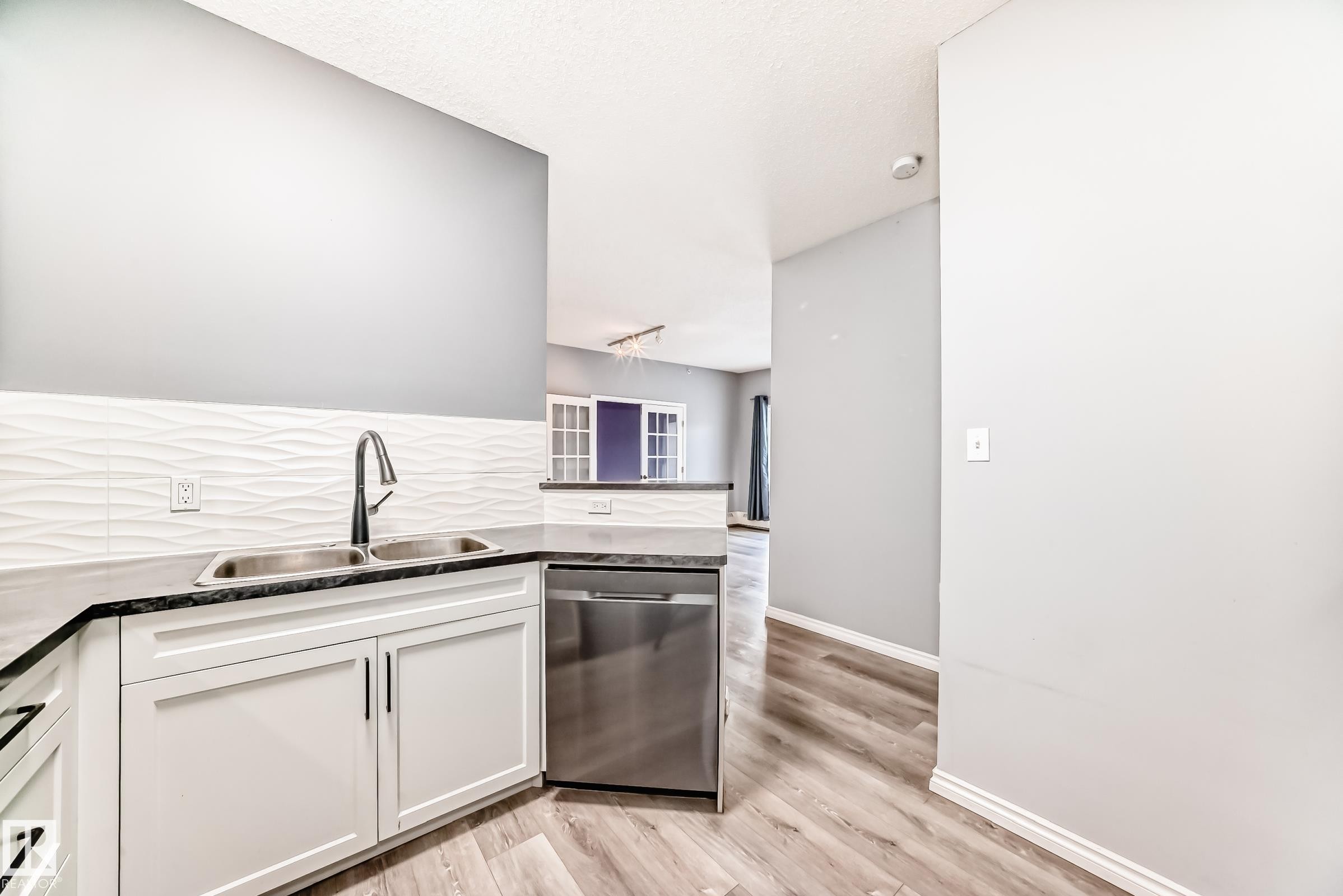 Kitchen featuring dishwasher, white cabinetry, light wood-style flooring, a peninsula, and dark stone countertops - 507 11716 100 Avenue, Edmonton, AB - Indoor Photo Showing Kitchen With Double Sink