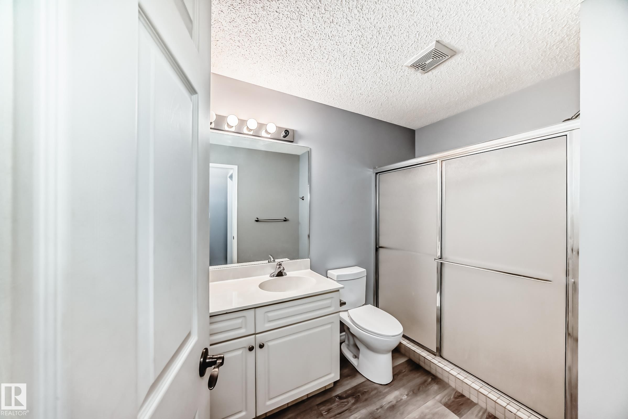 Bathroom with a textured ceiling, dark wood-type flooring, vanity, and a shower stall - 507 11716 100 Avenue, Edmonton, AB - Indoor Photo Showing Bathroom